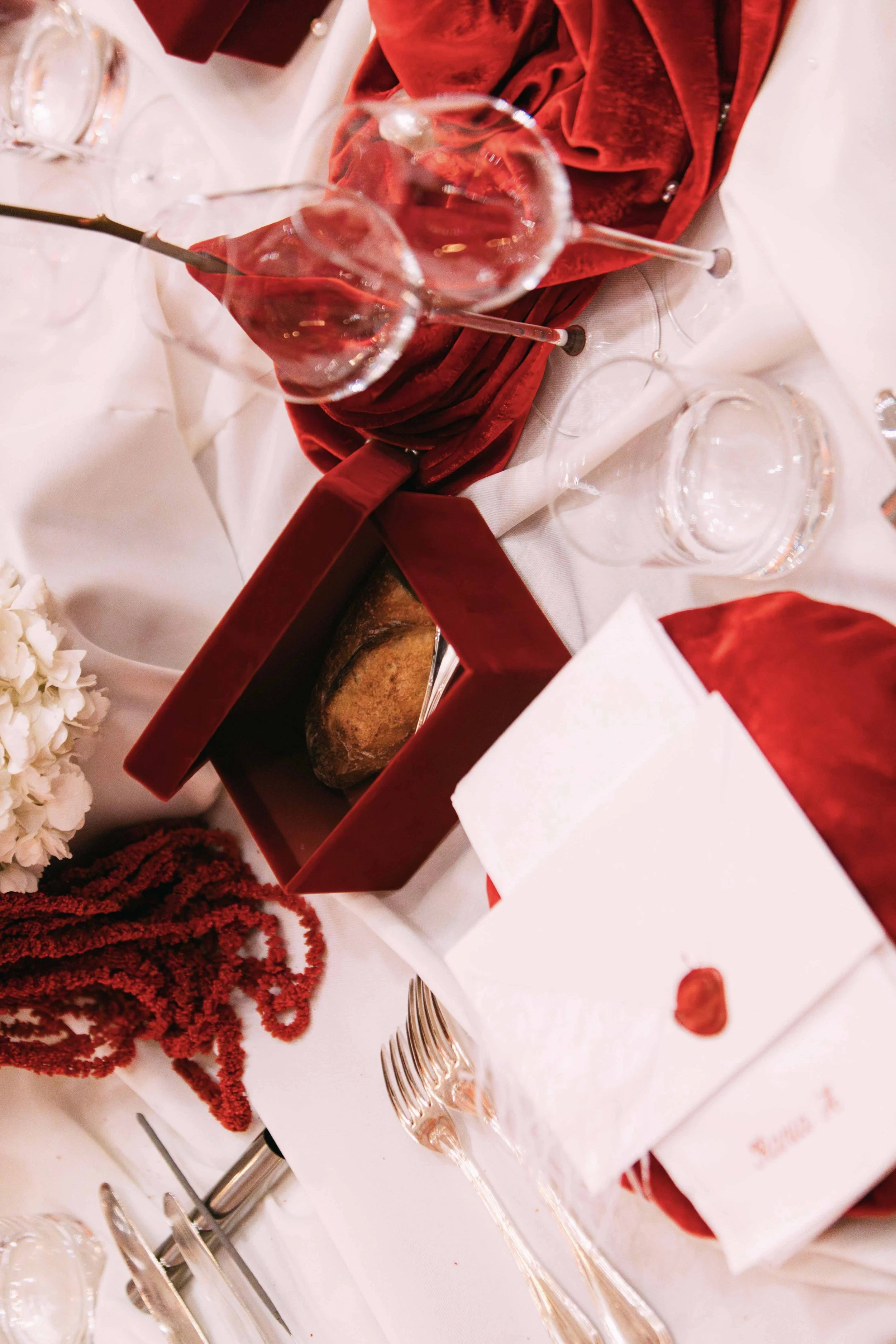 A decorated table with a red gift box containing bread, labels, wine glasses, and floral arrangements for a celebration or event.