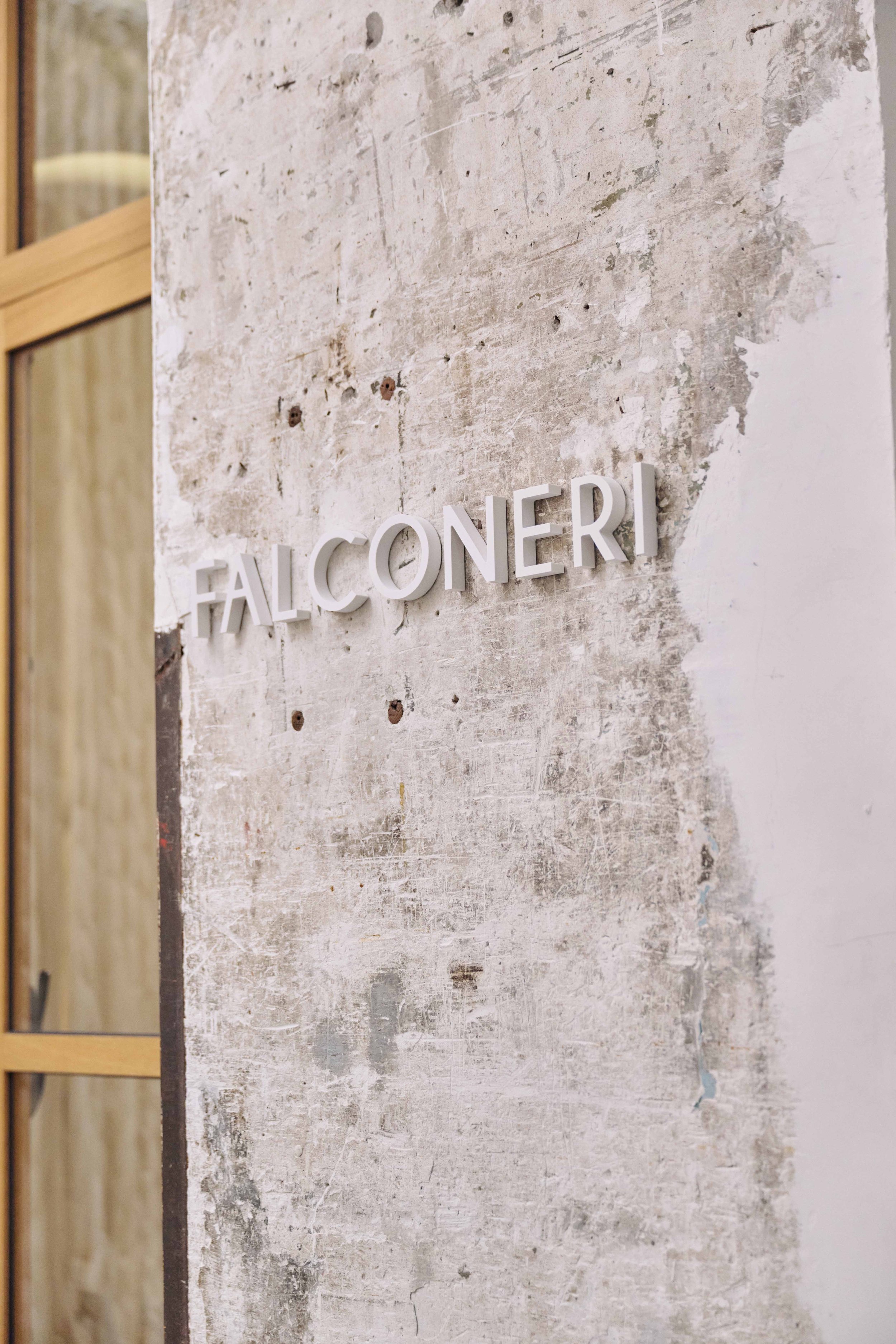 Close-up of a textured, worn concrete wall with white 3D letters spelling 'FALCONERI' attached to it.