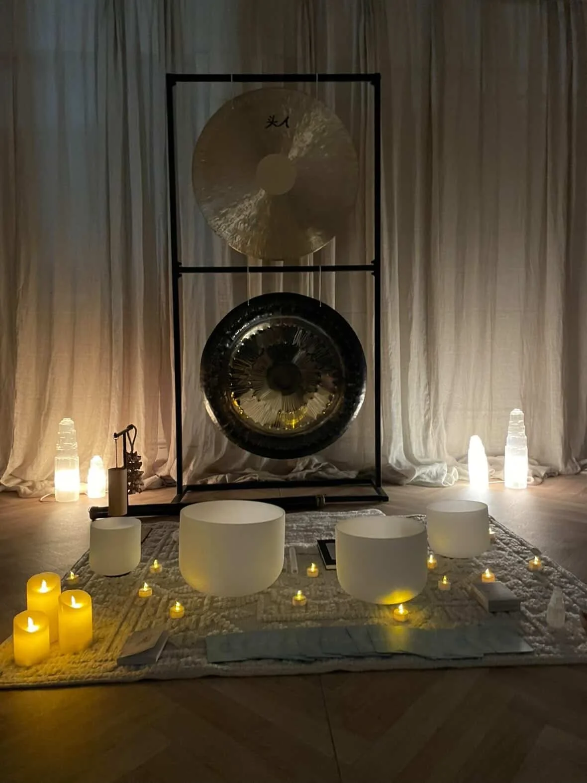 Decorative setup with candles, crystal singing bowls, and a gong on a stage with curtains in the background.