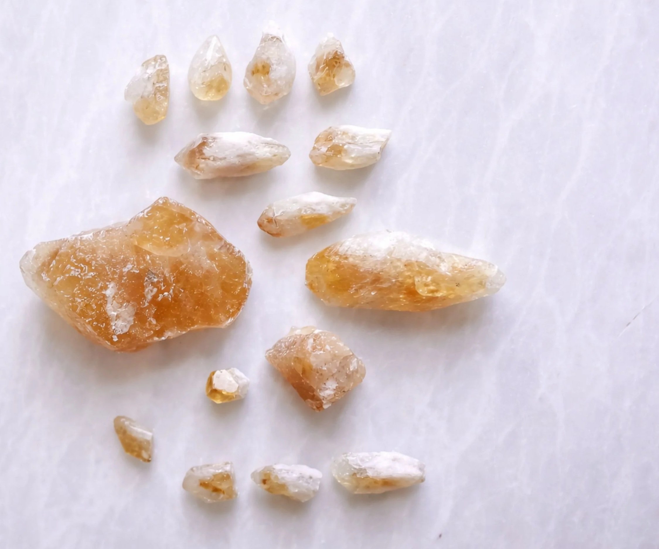 Fifteen rough citrine crystals on a white marble backdrop
