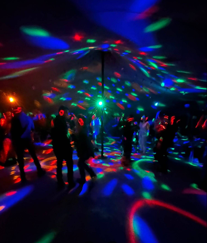 People dancing at a silent disco party under colourful, moving disco lights on the ceiling and floor.