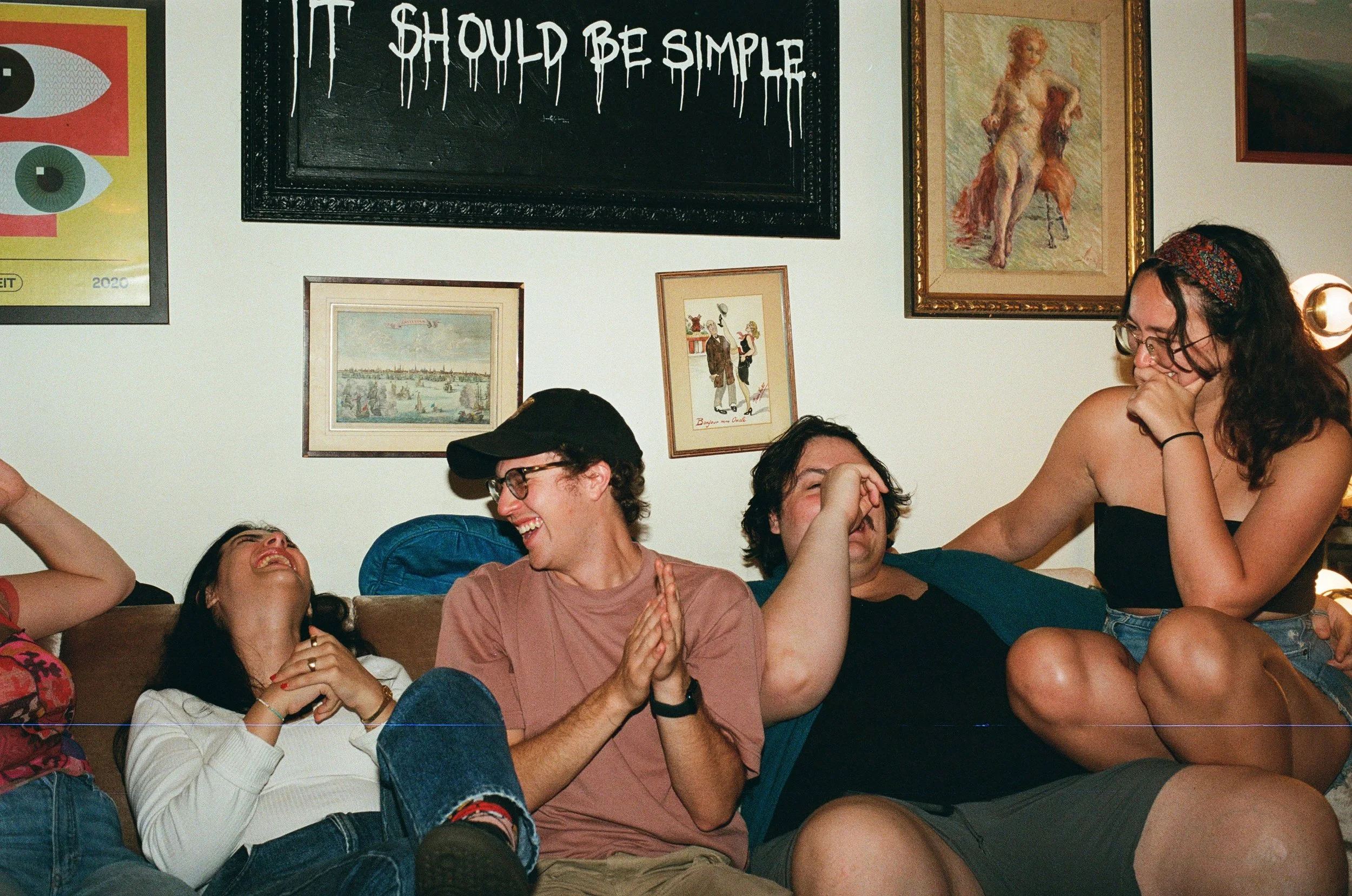 Group of young people laughing and enjoying each other's company in a living room with artwork on the wall behind them.