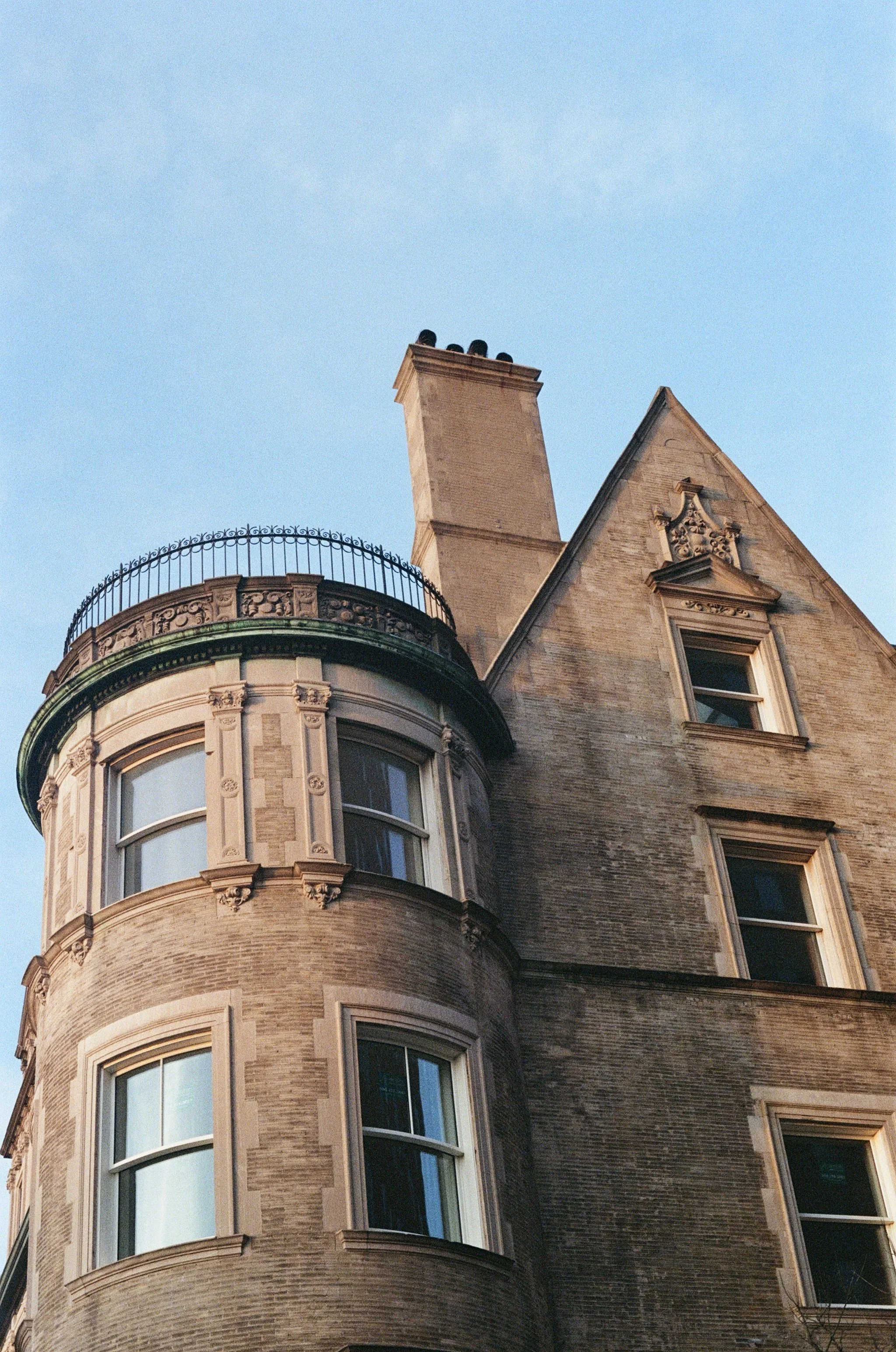 Close-up of a historic brick building with ornate window frames, a rounded turret with decorative molding, and a chimney against a clear blue sky.