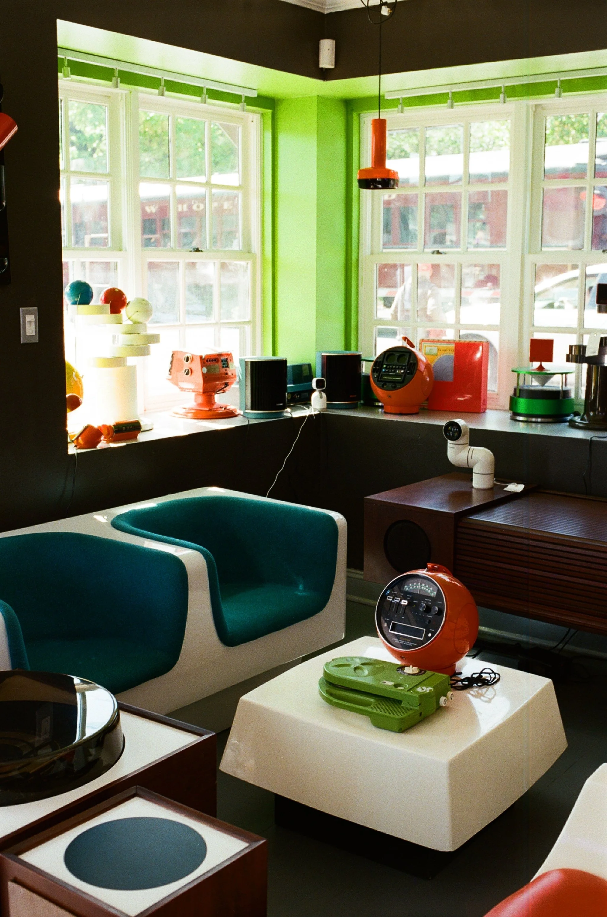 Interior of a modern retro-themed lounge or cafe with green walls, large windows, and vintage-style electronic devices and decorations.