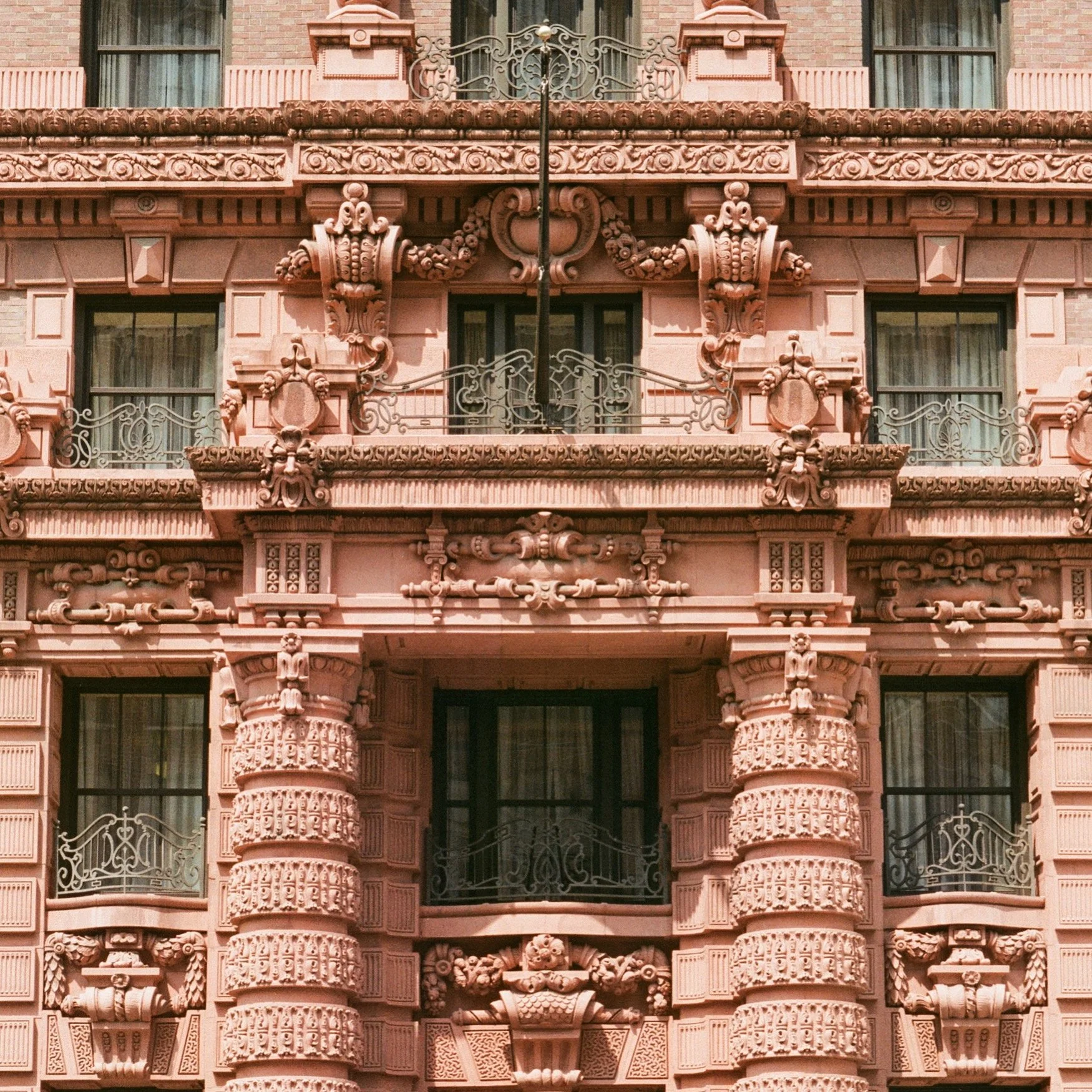 Facade of a pink ornate building with decorative columns, balconies with wrought iron railings, and detailed architectural carvings.