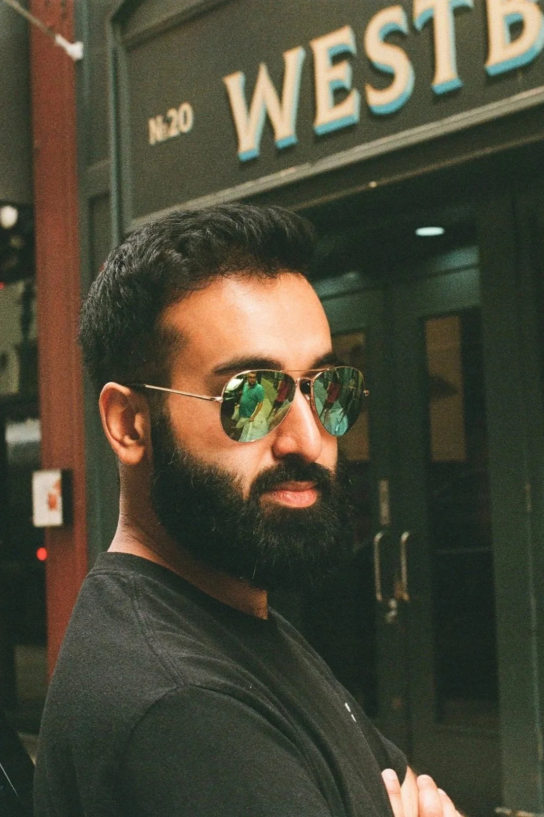 A man with dark hair, a beard, and sunglasses standing in front of a store named Westside.