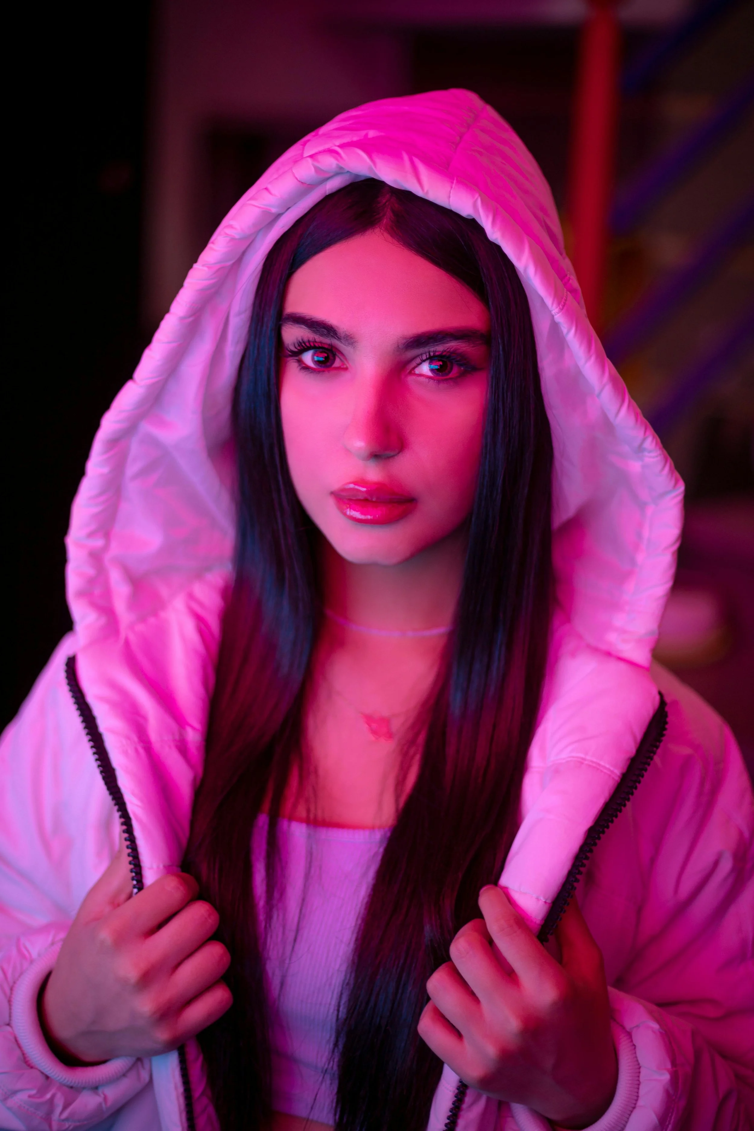 Image of a young woman with pink neon lighting reflecting on her face, well lit professonal studio shot, as part of a video camapign in Manchester