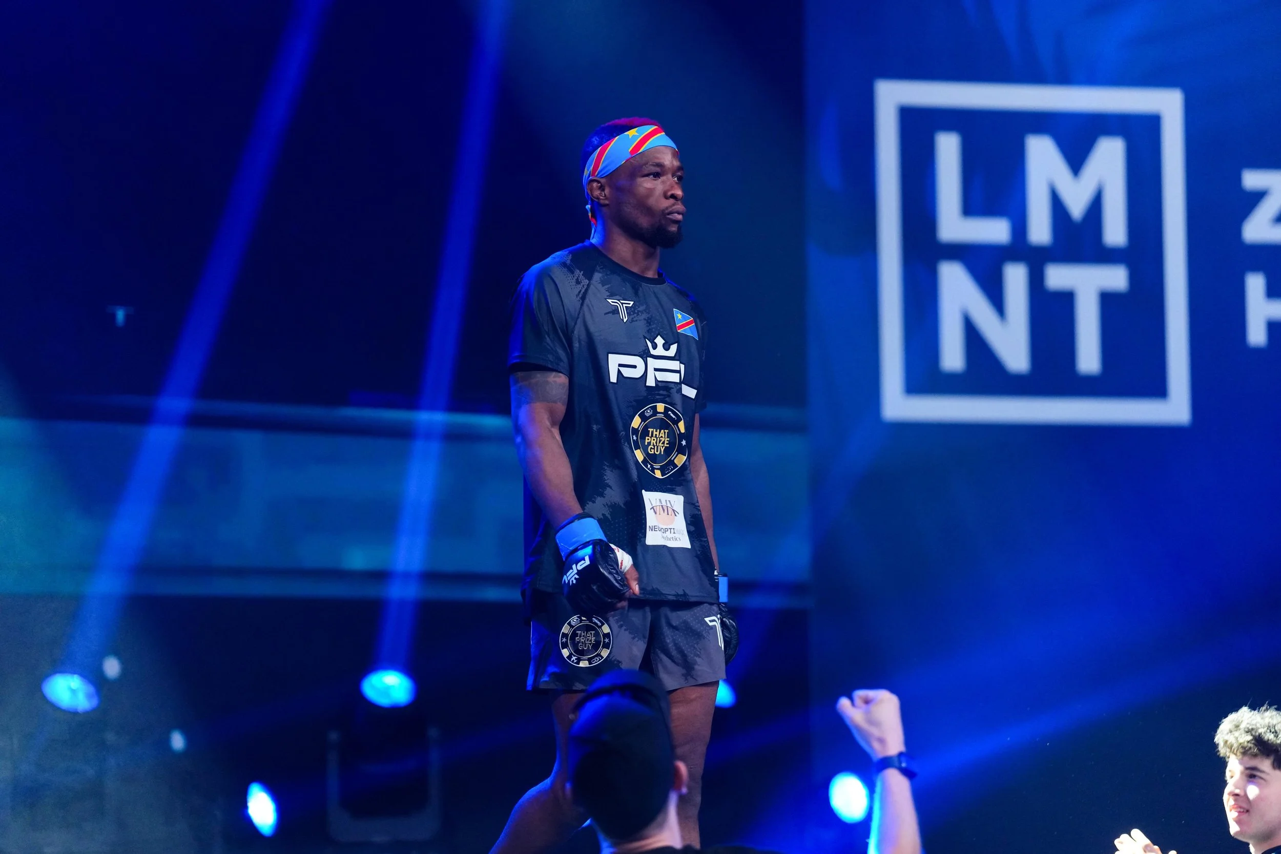 Image of marc diakiese walking on stage at a PFL event, wearing a tshirt that says "sponsored by made by uno - brand and video studio in Doncaster"