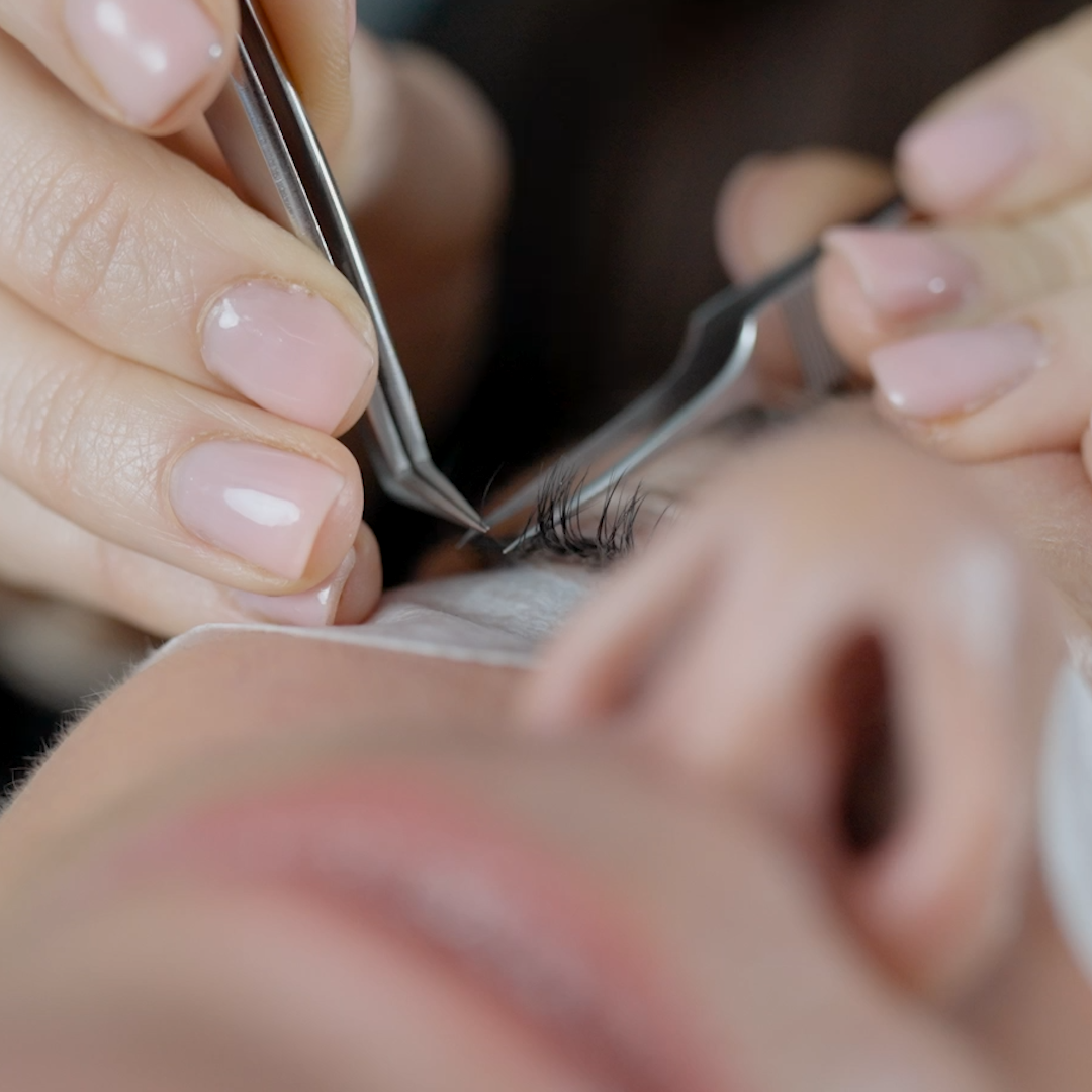 Close-up of a person's eye being eyelash extension applied by a Creative Quarter technician using tweezers.