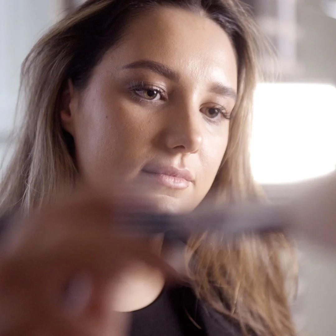 A brand shoot of a woman with light brown hair and light makeup applying makeup to a model at creative quarter in doncaster, with a soft expression.