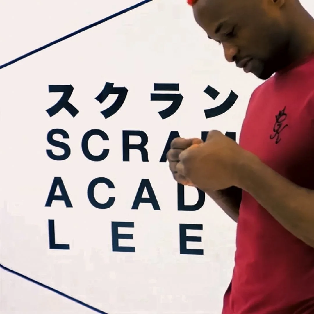 Marc Diakiese in a red shirt, infront of a sign reading "scramble academy leeds"