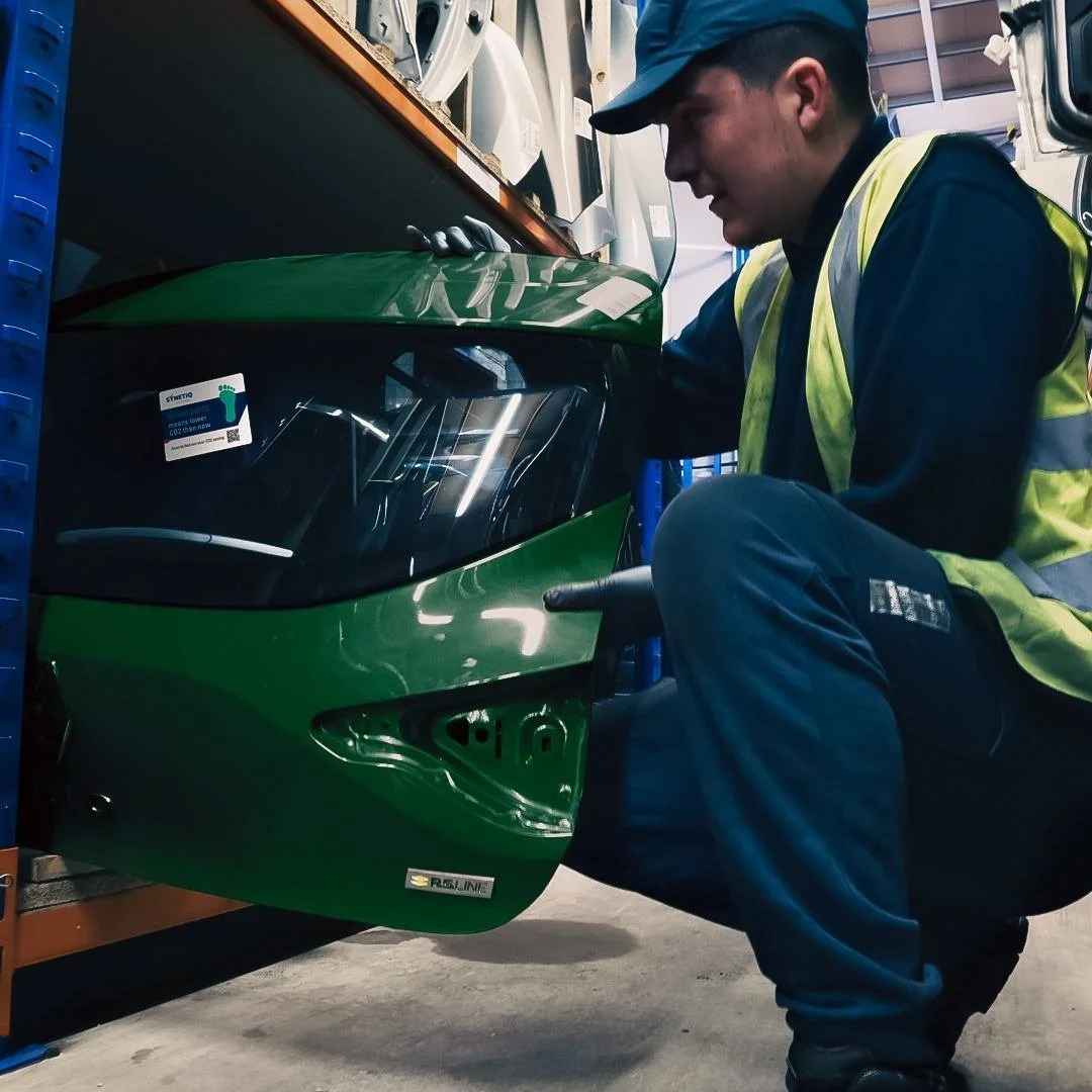 A worker inspecting a green vehicle on a shelf at Synetiq warehouse in Doncaster, wearing a yellow safety vest and gloves