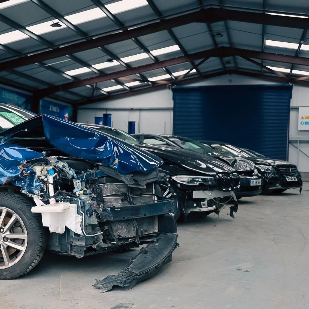 Indoor car salvage lot with several damaged vehicles at Synetiq warehouse in Doncaster, including a blue car with front-end damage, and other black cars parked in a row.