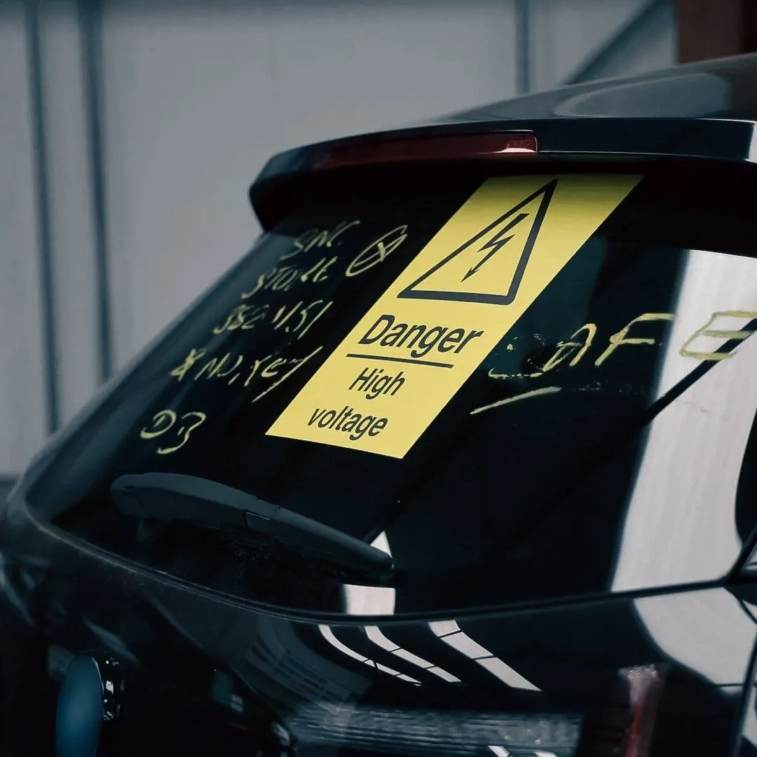 Close-up of an electric vehicle with a yellow caution sticker warning of high voltage and danger.