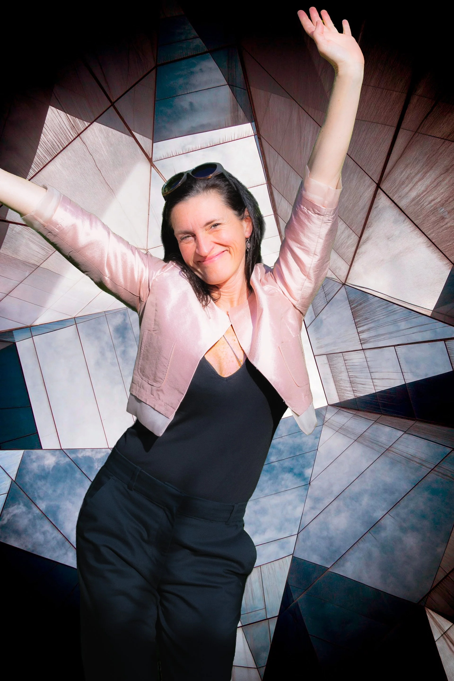 Vrouw met opgeheven armen die vrolijk poseert voor een geometrische architecturale achtergrond.