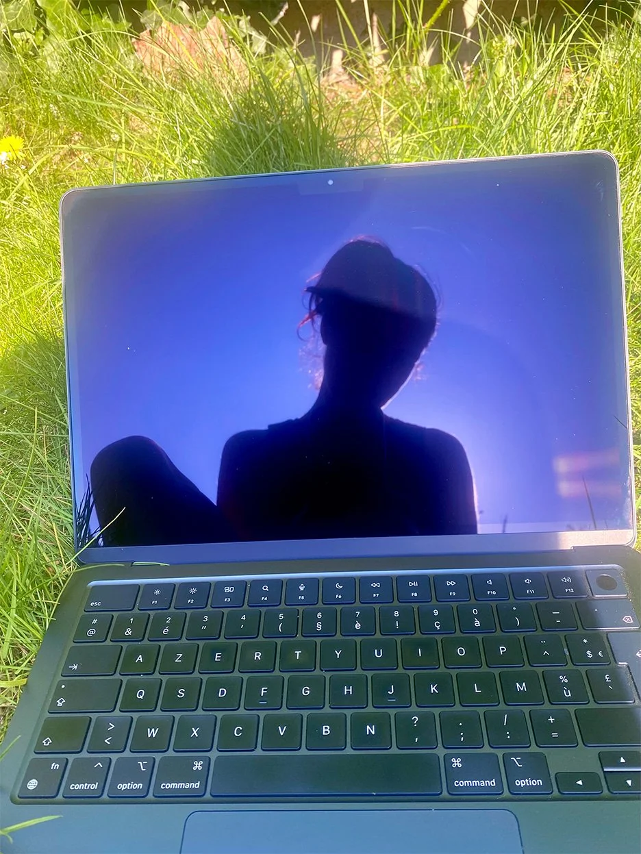 Reflectie van Katty op een laptopscherm in het gras als symbool voor persoonlijk contact en verbinding.