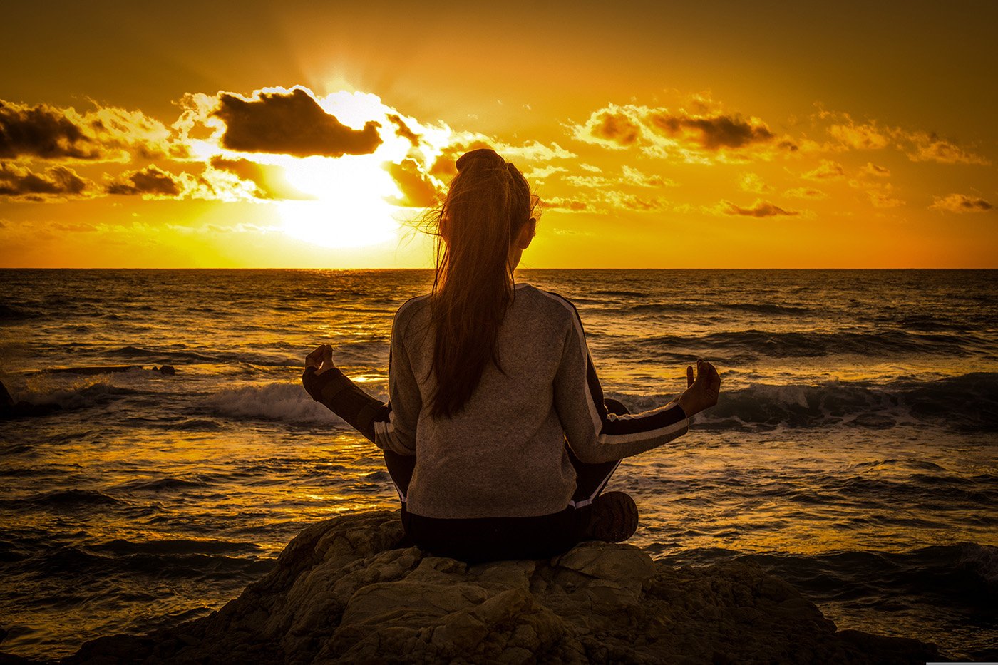 Persoon die mediteert aan zee bij zonsondergang als symbool voor rust en herstel van energie