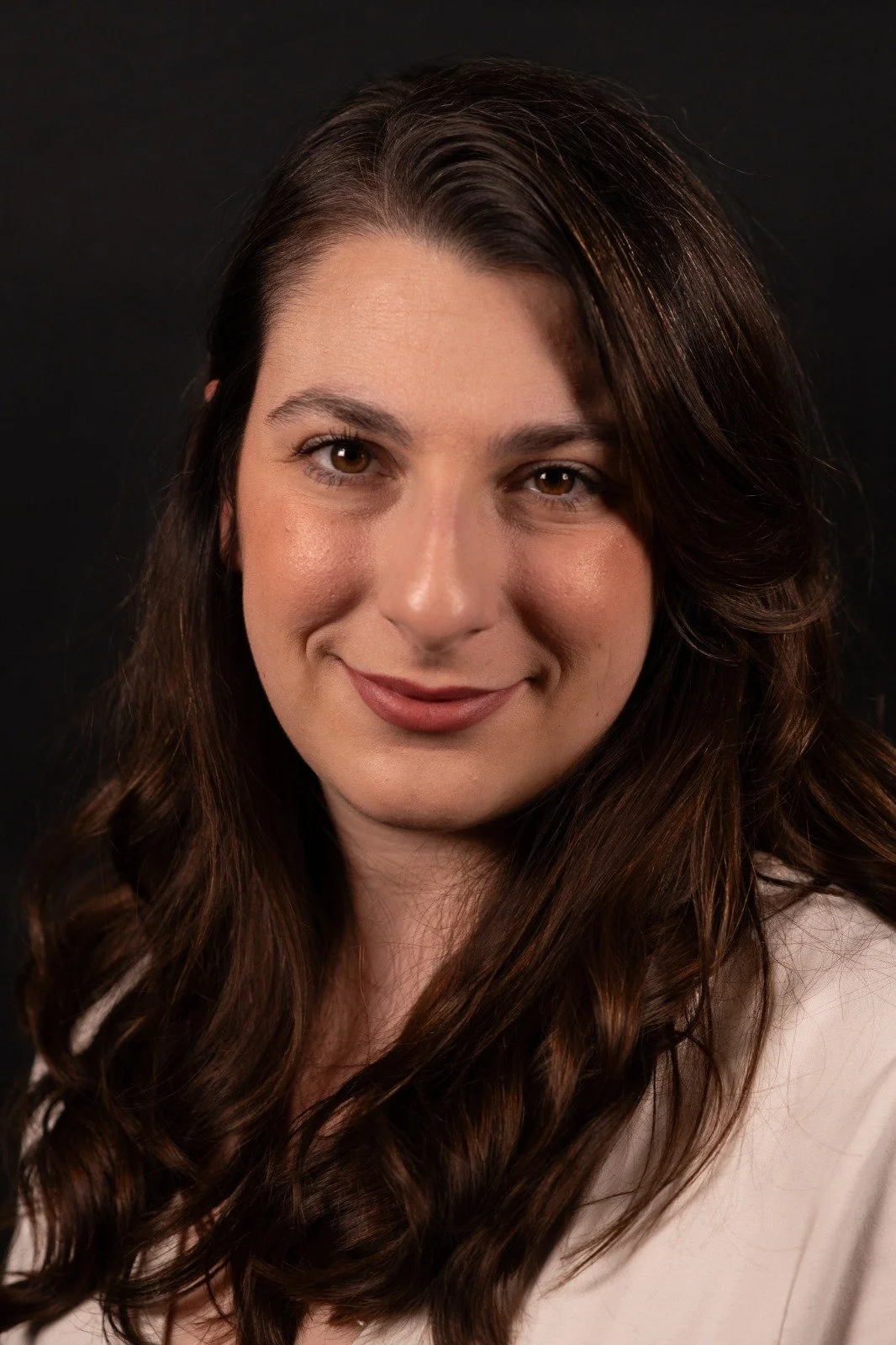 Mina Murat Baldwin, BACP registered therapist, Close-up with long, wavy brown hair and light skin, smiling softly against a dark background.