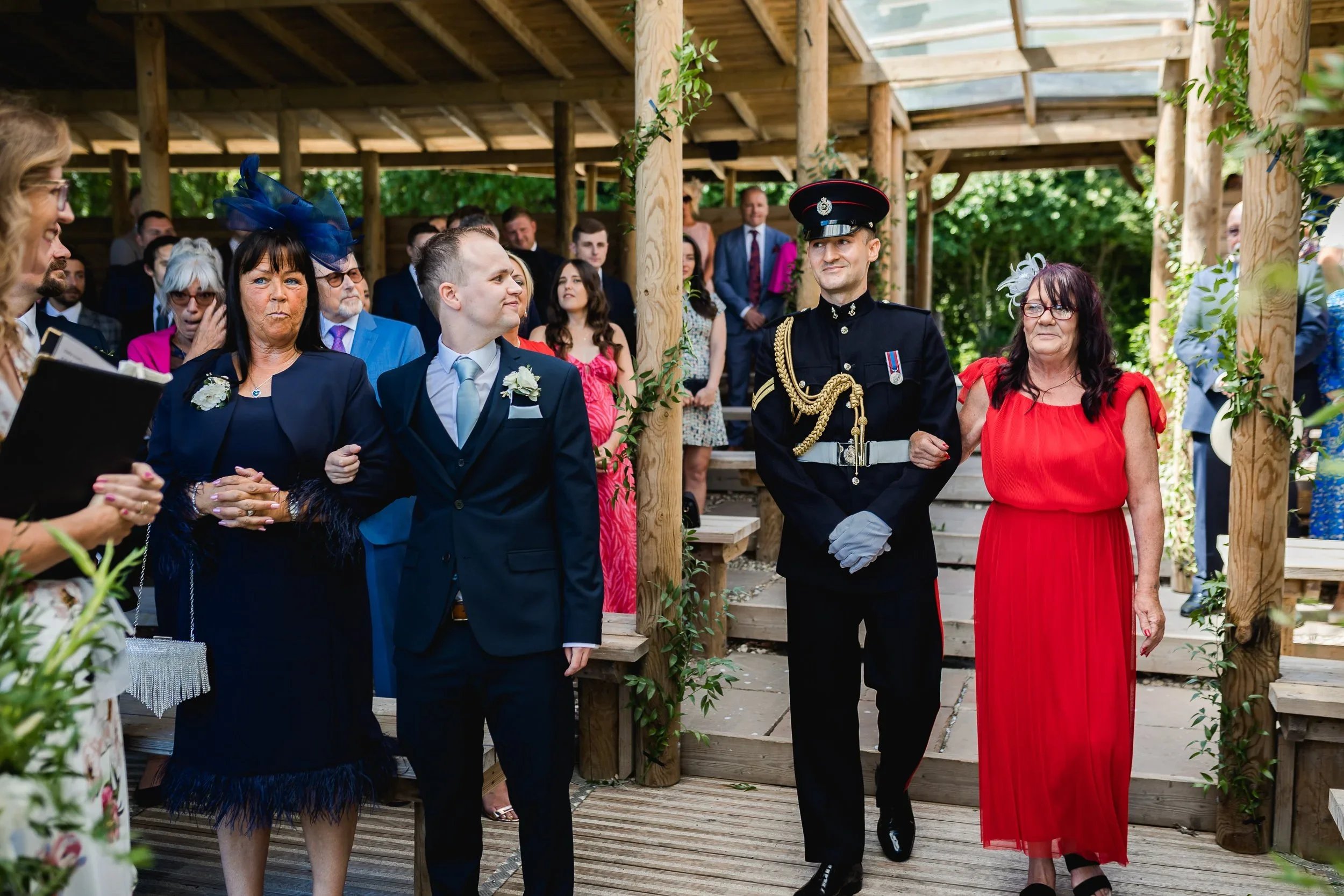 Groom walking down the aisle with family during an outdoor wedding ceremony in the lakeside pavilion at Oaklands Grand Lodge in Driffield, East Yorkshire.