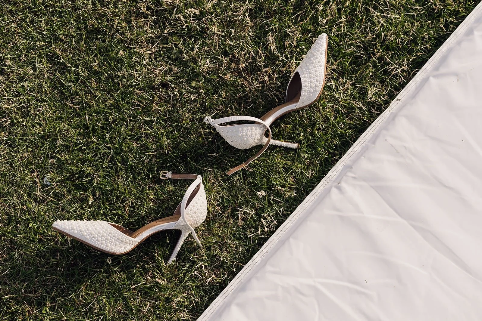 Ivory bridal heels resting on the lawn beside Becky’s wedding dress