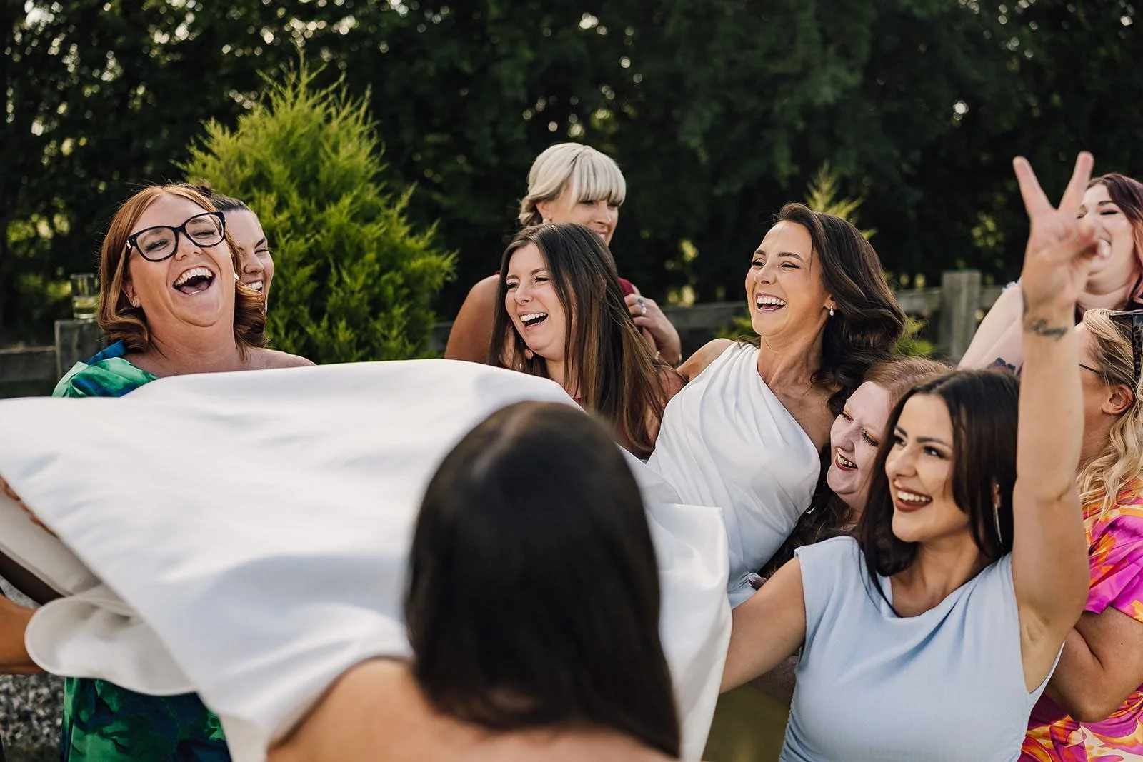 Wedding guests laughing together beneath Becky’s veil in the garden