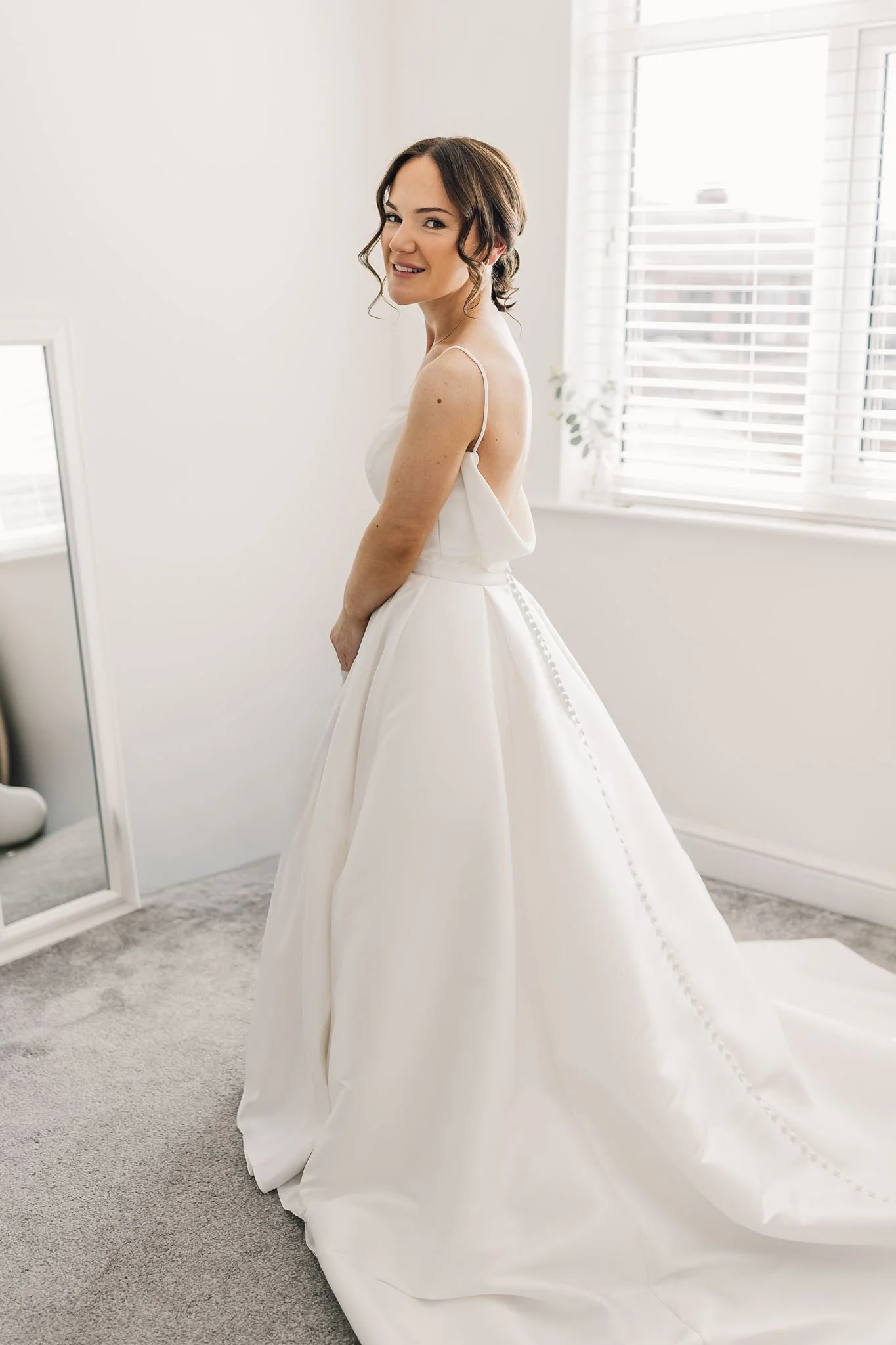 Rachel standing by a window in her wedding dress