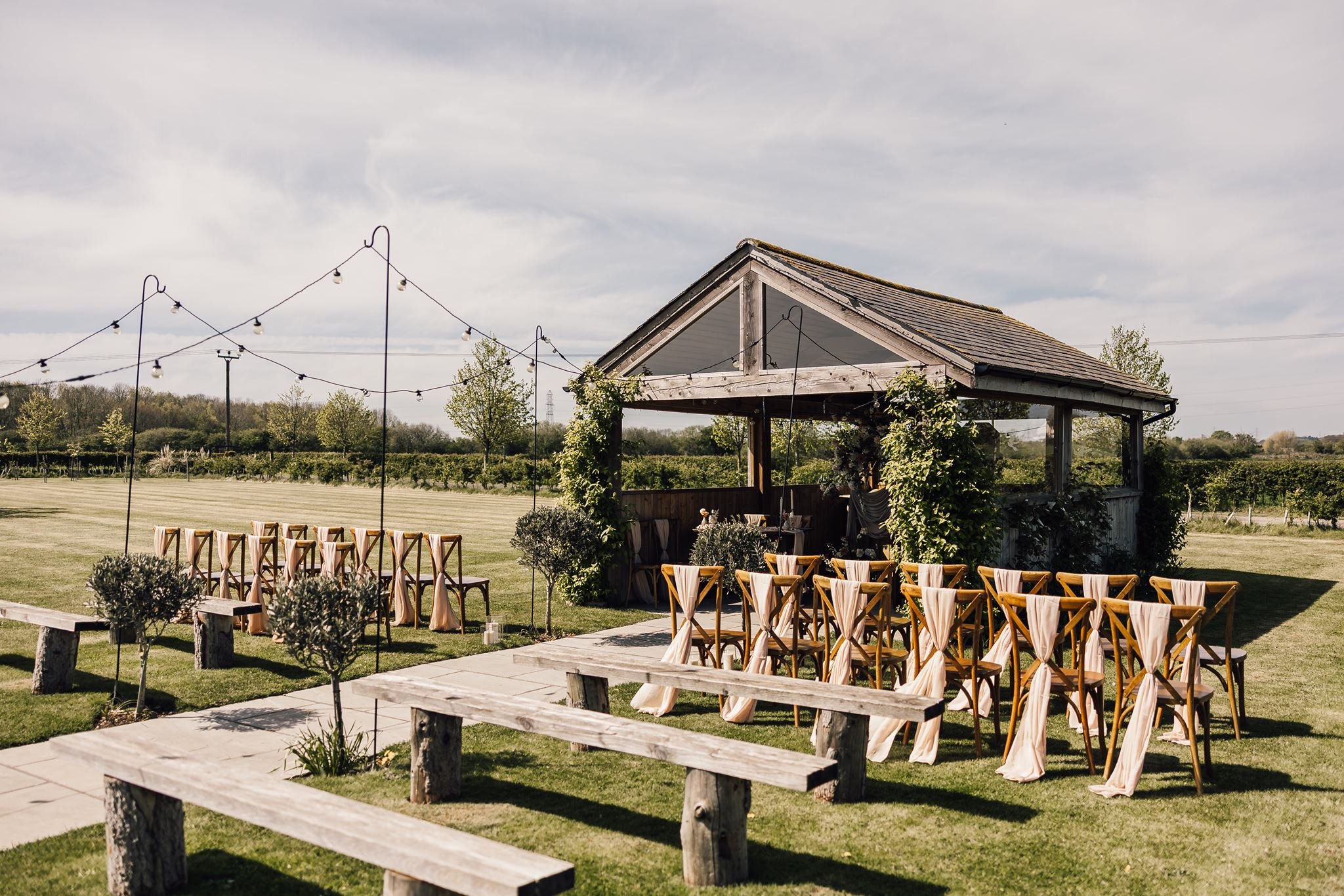 Outdoor ceremony chairs and festoon lights in the gardens at The Beverley Barn