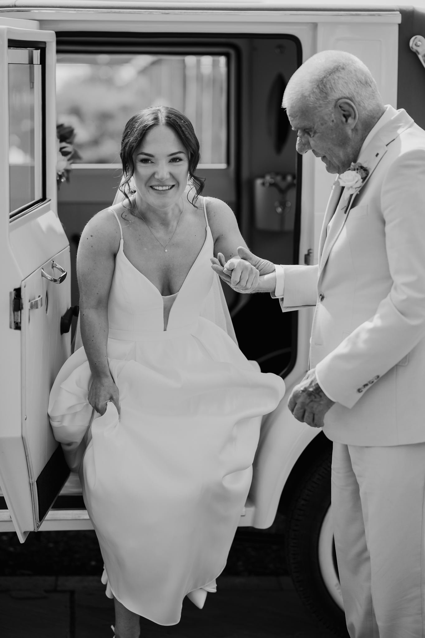 Rachel stepping out of the wedding car with her dad, in black and white