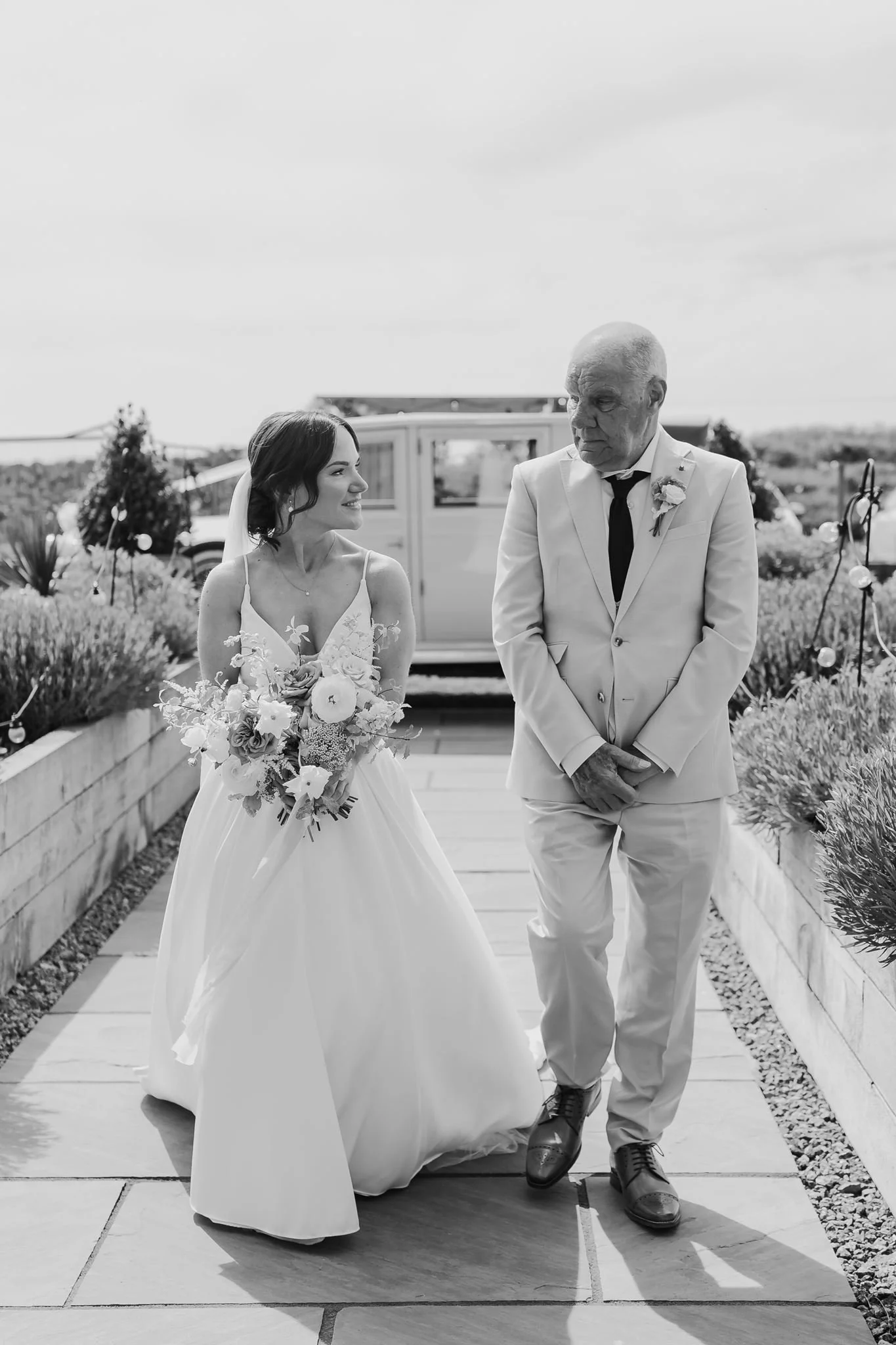 Rachel walking with her dad towards the outdoor ceremony, in black and white