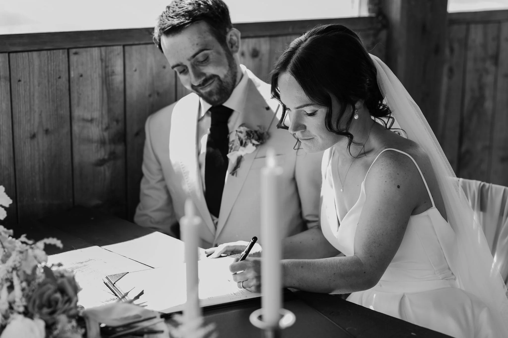Rachel signing the marriage paperwork with Harry beside her, in black and white