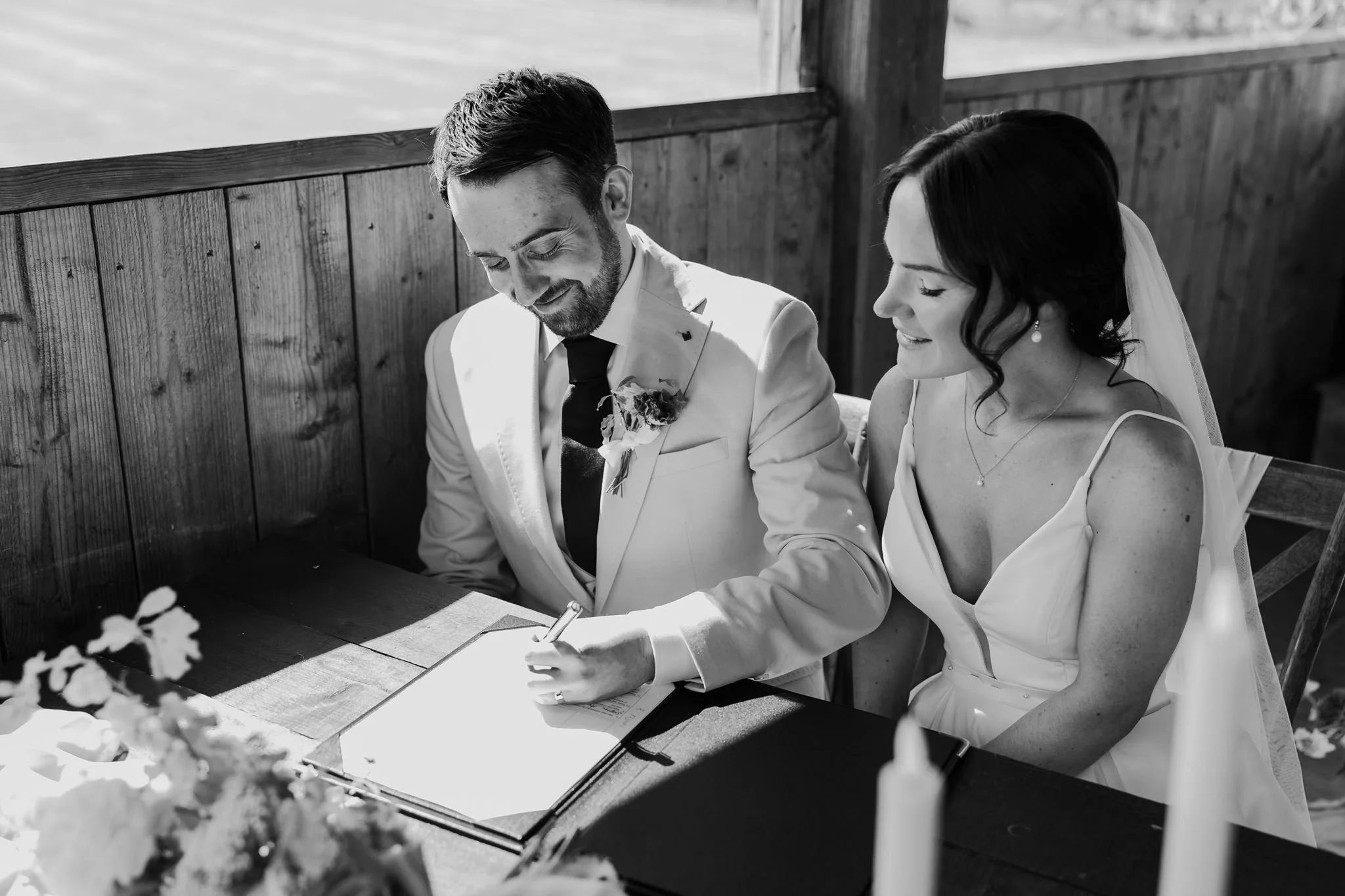 Harry signing the marriage paperwork while Rachel watches, in black and white