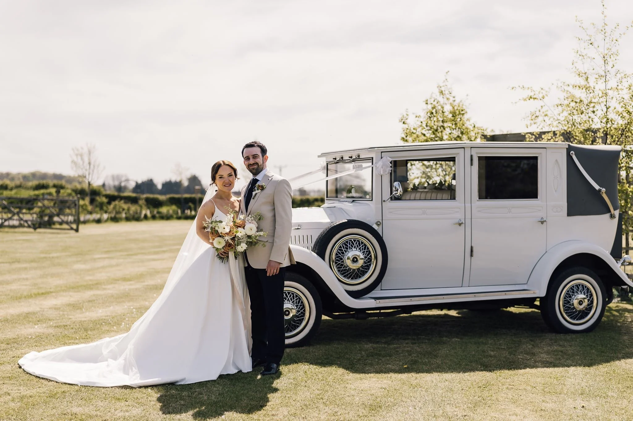 Rachel and Harry standing beside their vintage wedding car