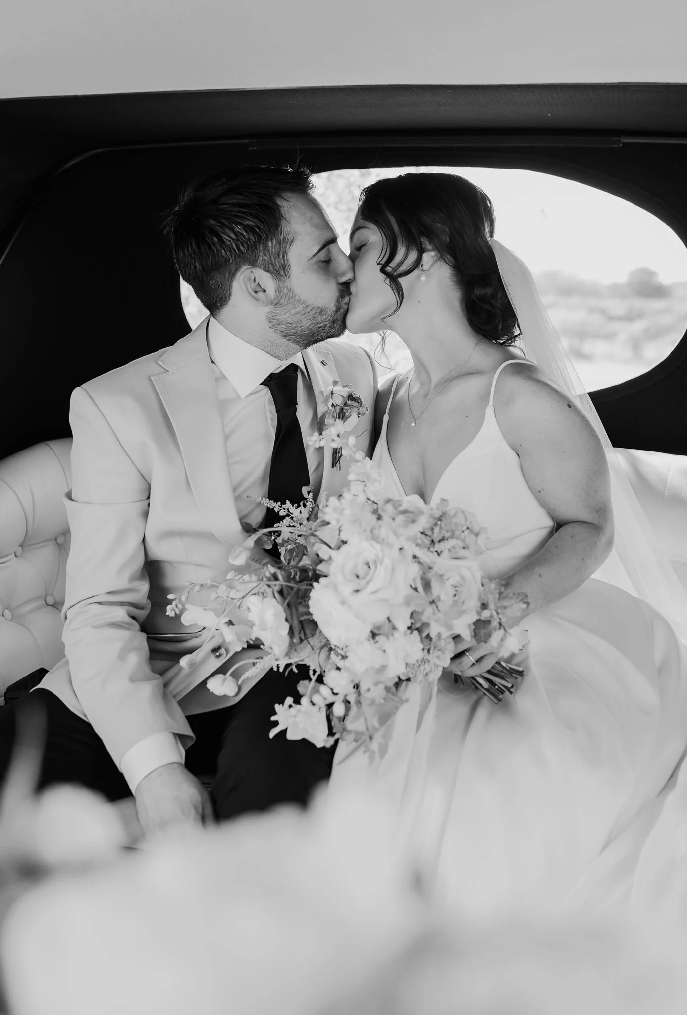 Rachel and Harry kissing inside their wedding car, in black and white