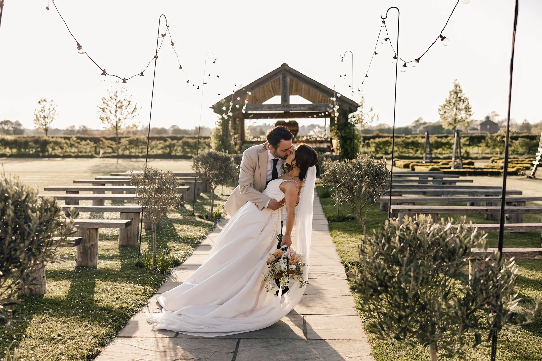 Rachel and Harry sharing a kiss on the garden path beneath festoon lights