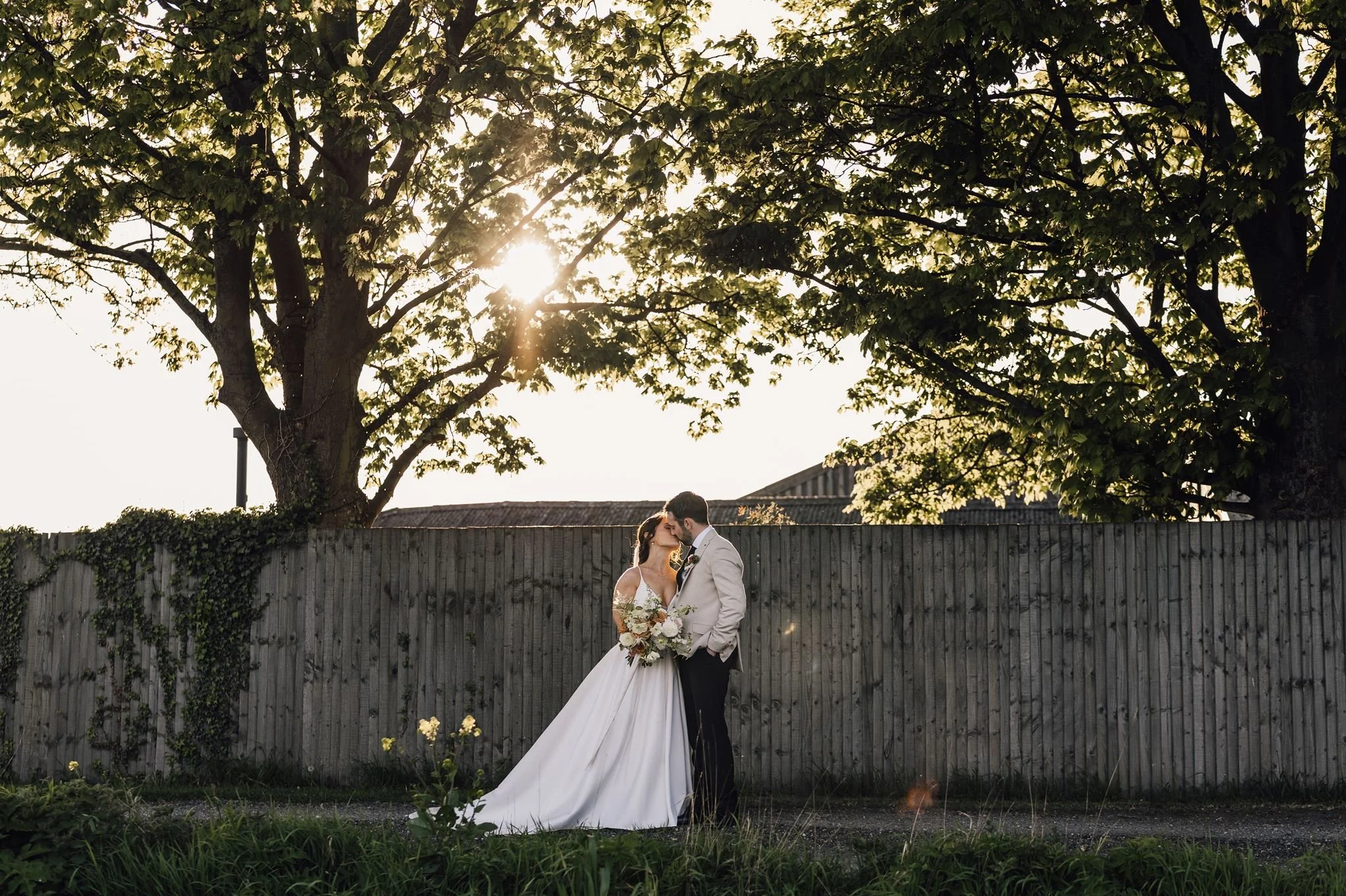 Rachel and Harry embracing beneath a tree in the evening sunshine
