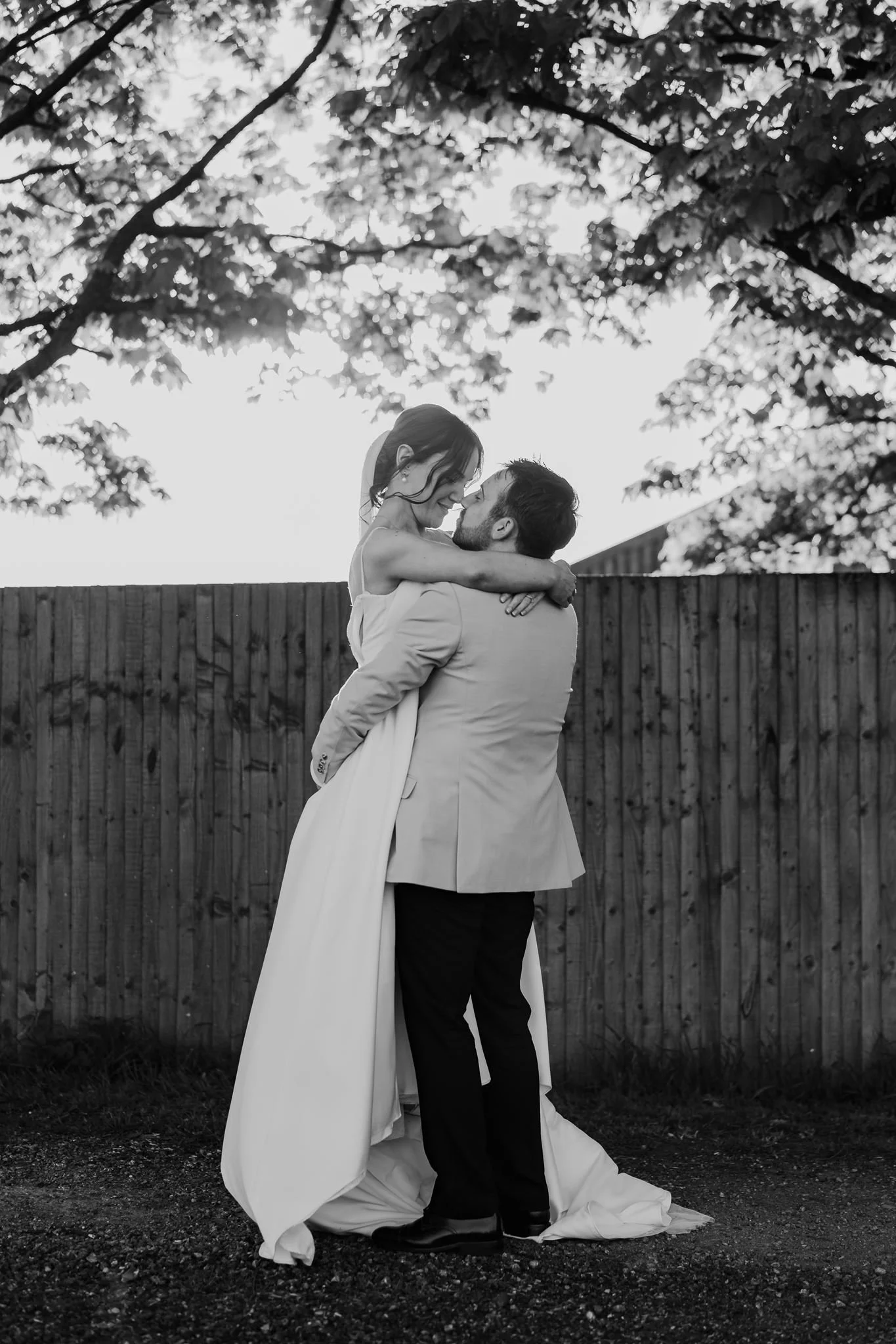 Rachel and Harry sharing a kiss beside a wooden fence, in black and white