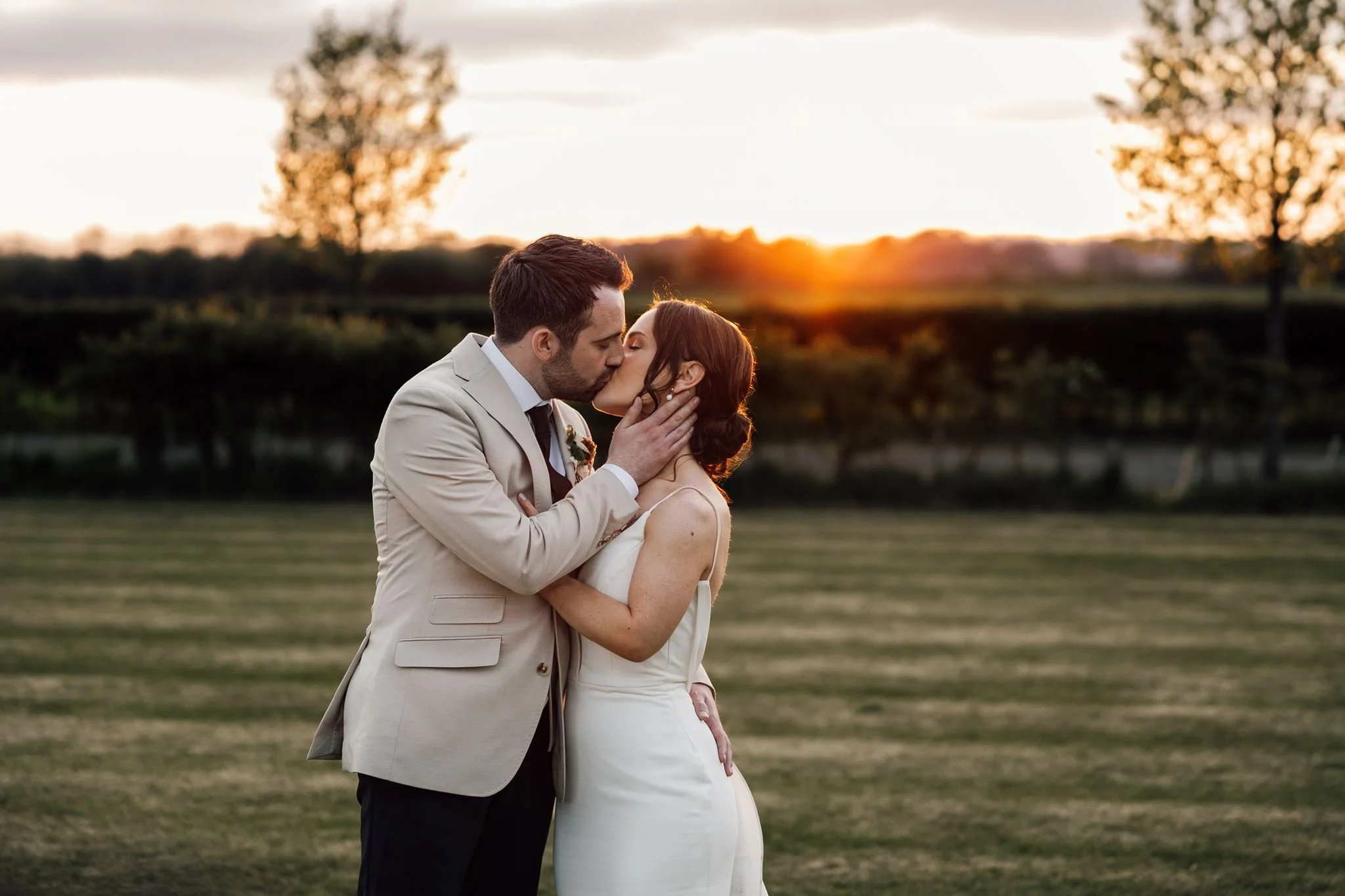 Rachel and Harry kissing as the sun sets over the fields
