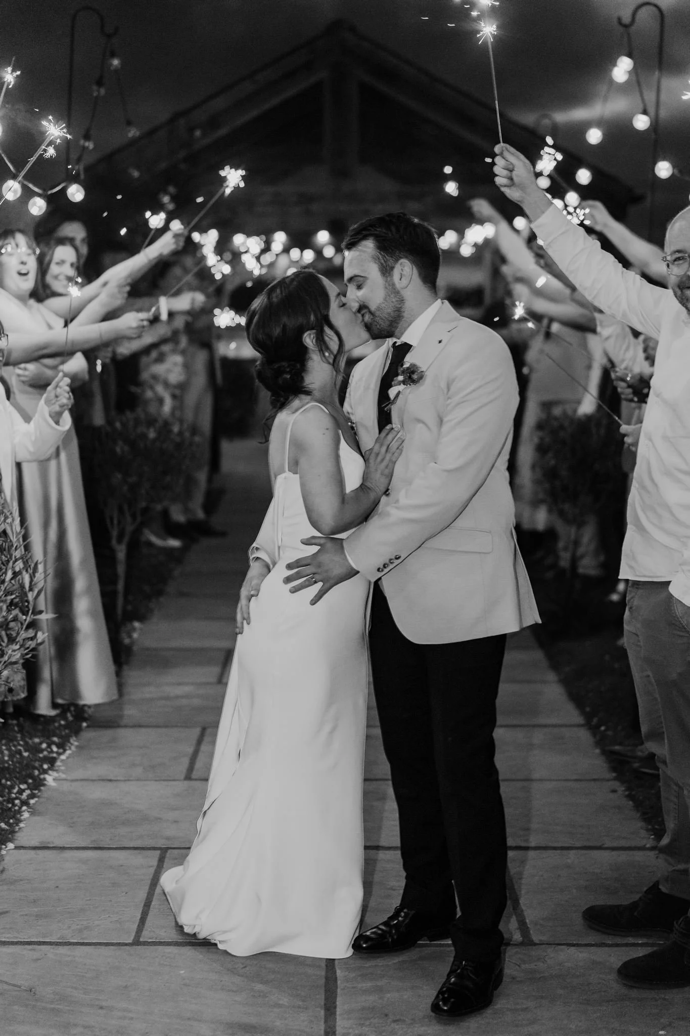 Rachel and Harry surrounded by guests holding sparklers, in black and white