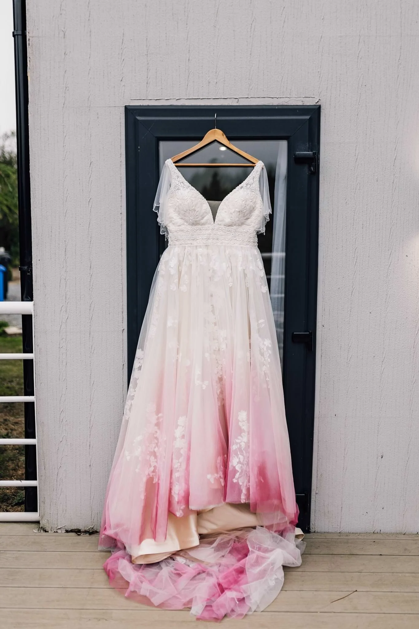 Wedding dress with a pink hem hanging in a doorway before Chloe and Aaron’s wedding