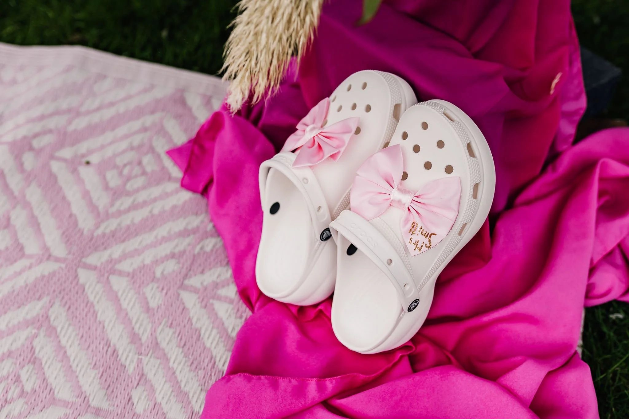 Decorated white wedding Crocs beside pink fabric