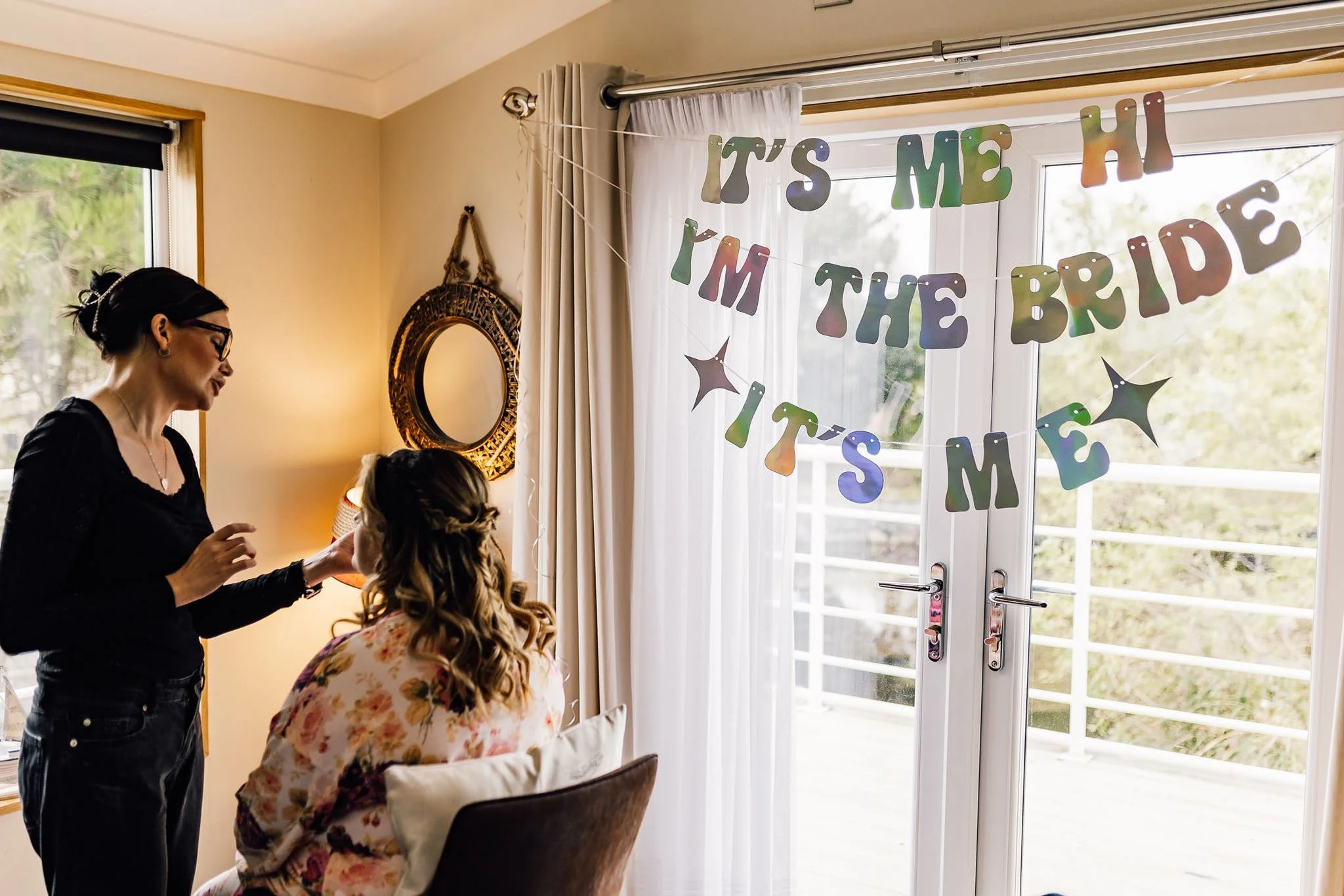 Chloe having her hair styled beside an ‘It’s me, hi, I’m the bride’ banner