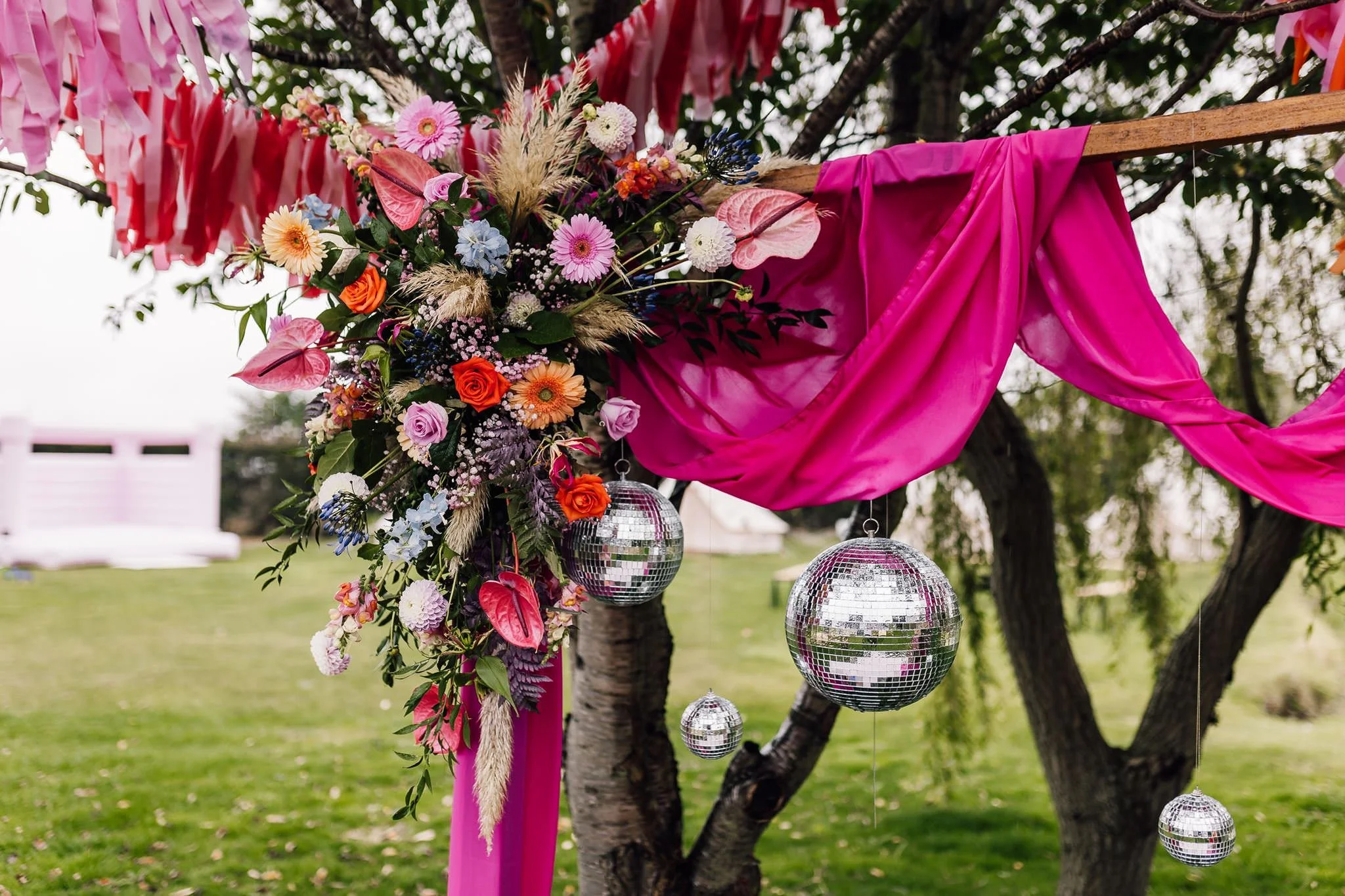 Colourful flowers, pink fabric and a disco ball decorating the ceremony arch
