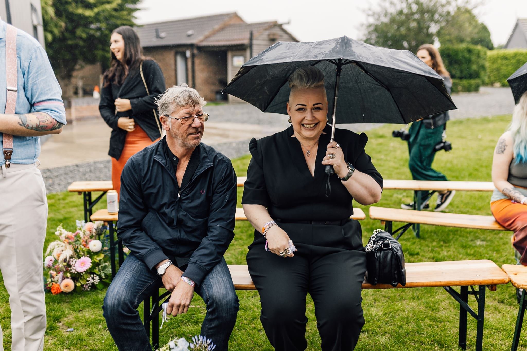 Two wedding guests watching the ceremony under an umbrella