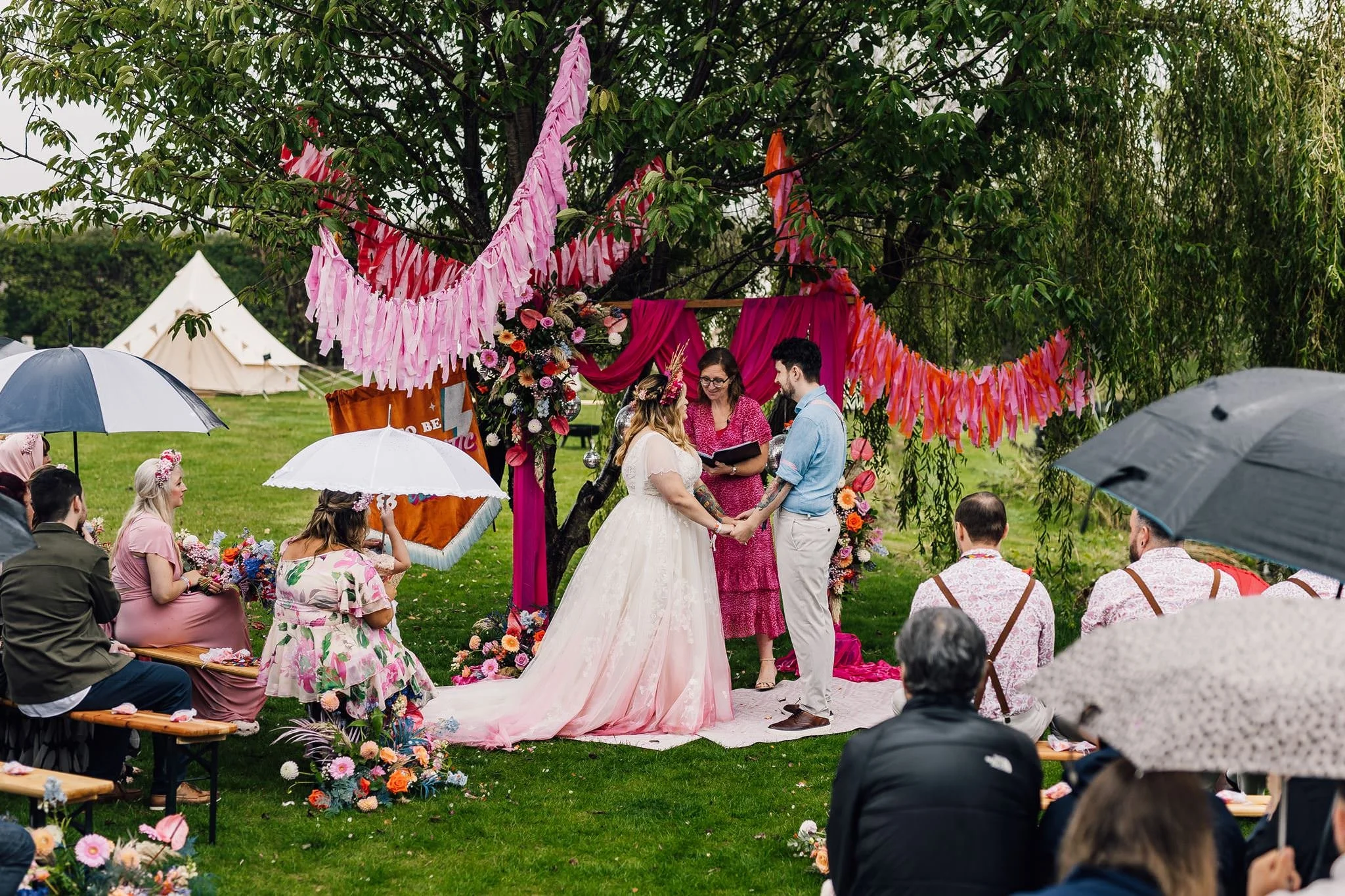 Guests with umbrellas watching the outdoor festival wedding ceremony at Pitch 21