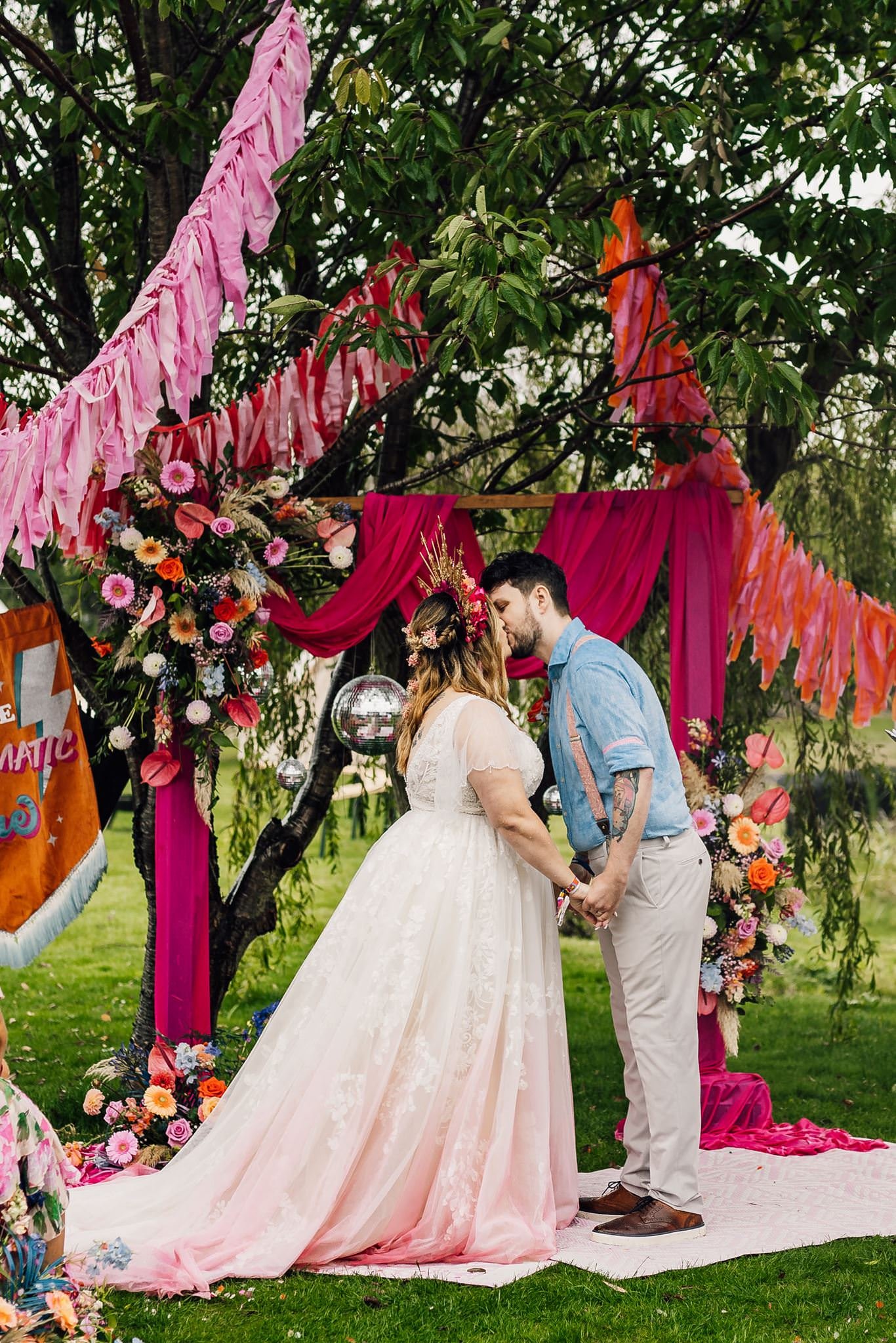 Chloe and Aaron kissing beneath the pink-draped floral ceremony arch