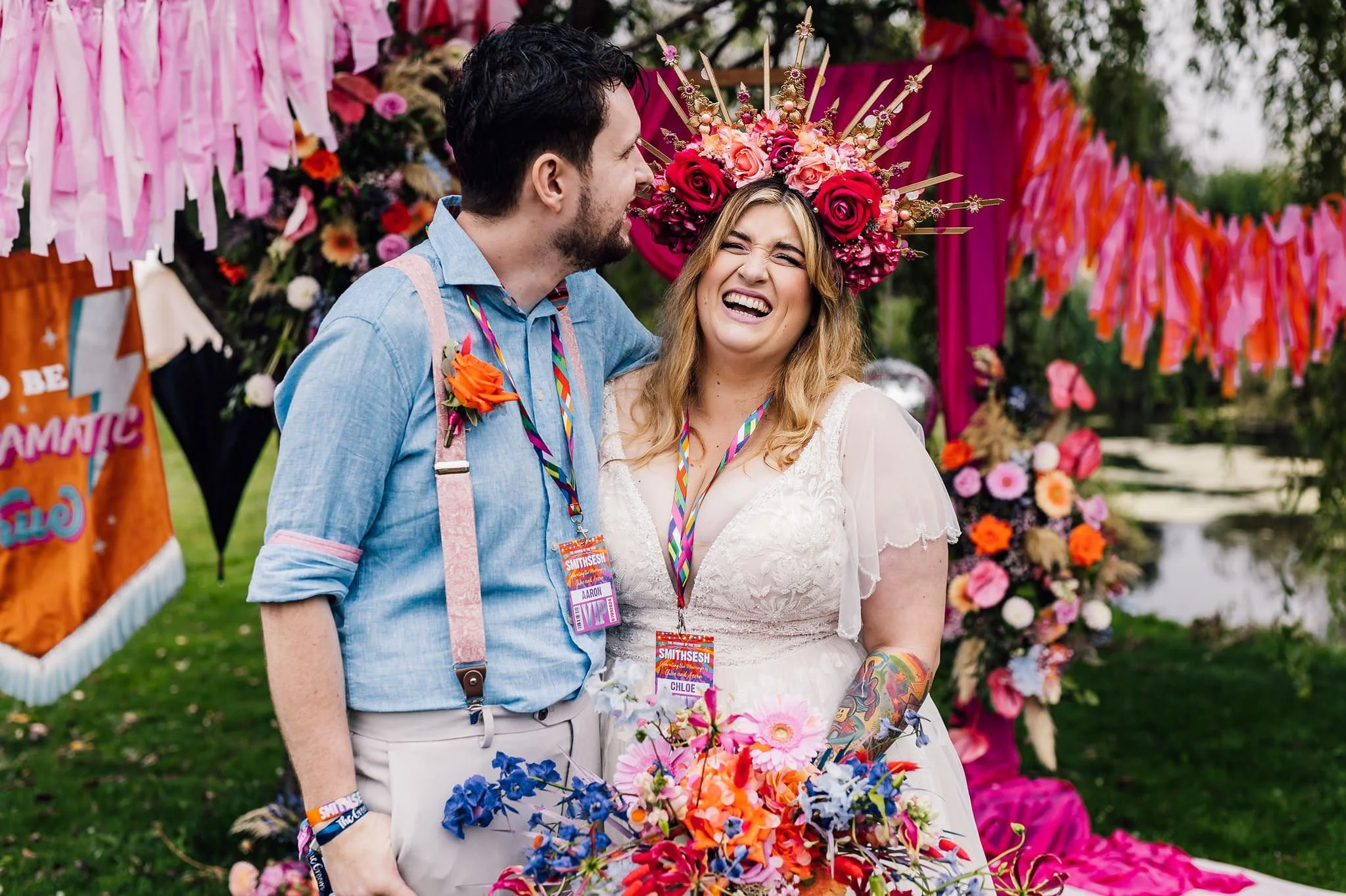 Aaron kissing Chloe’s cheek as she laughs beneath colourful wedding decorations