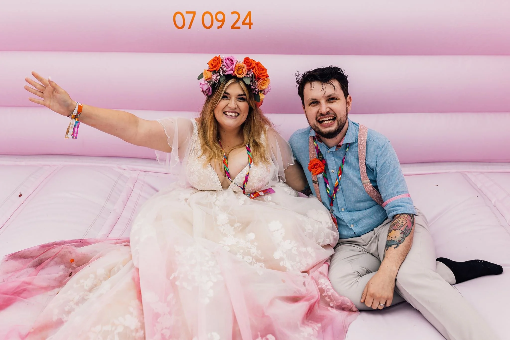Chloe and Aaron laughing together on a pink bouncy castle at their festival wedding