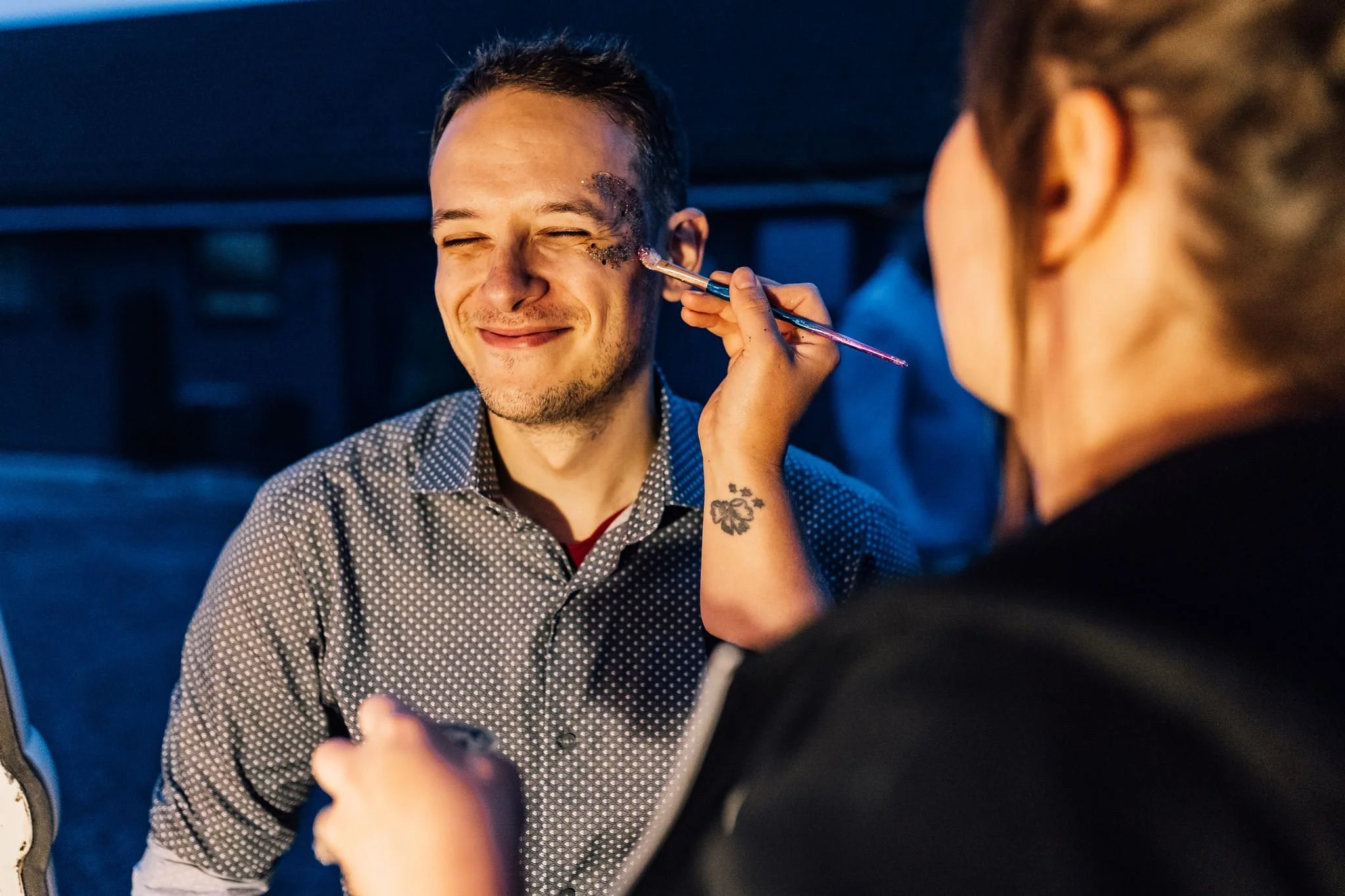 A wedding guest having glitter applied to his face
