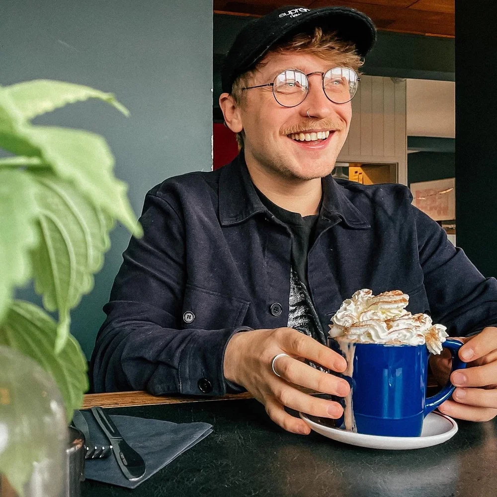 Dan from Dandrew Photography, wearing his cap and glasses and smiling over a mug