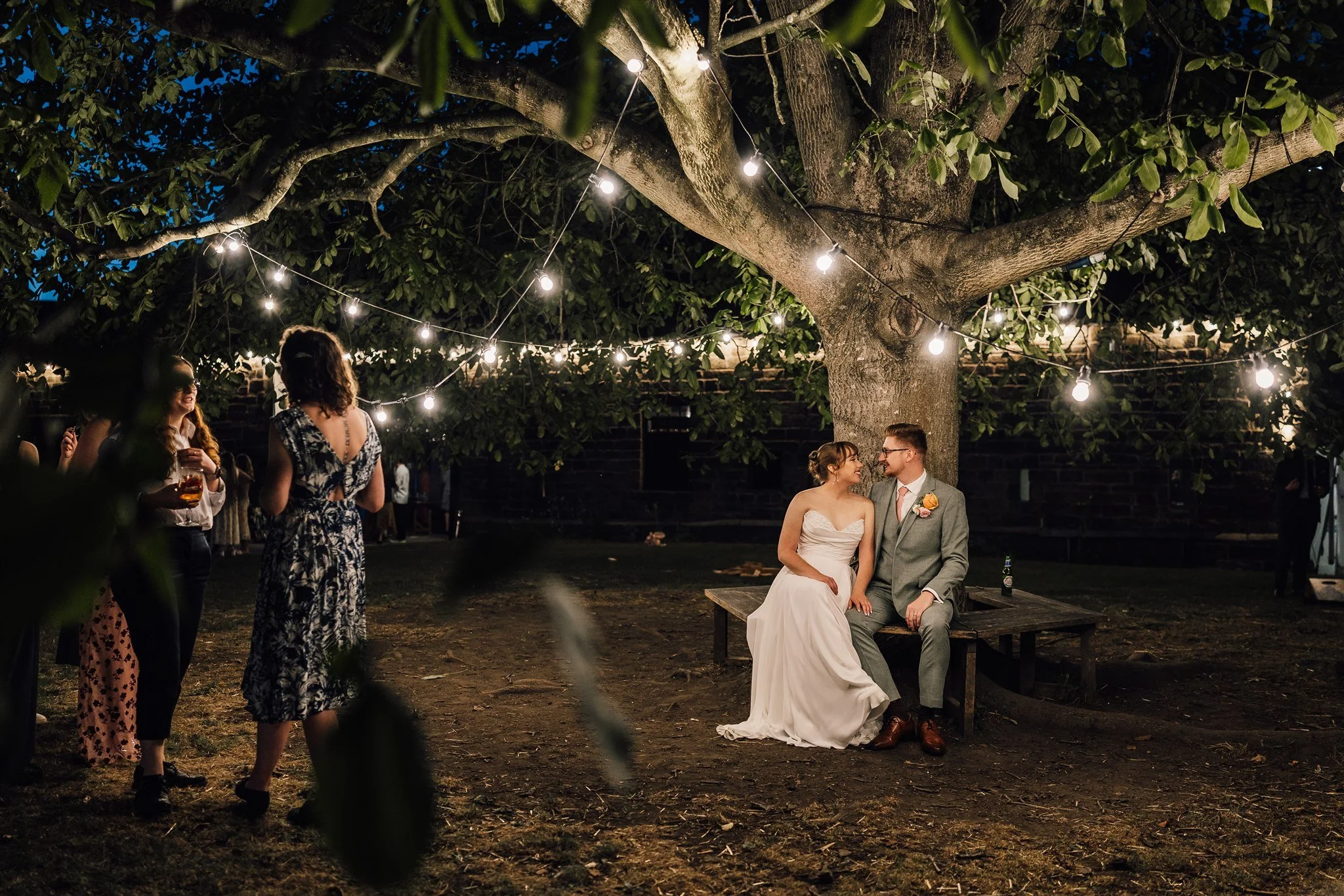 Bride and groom sitting under festoon lights in the evening at East Riddlesden Hall wedding